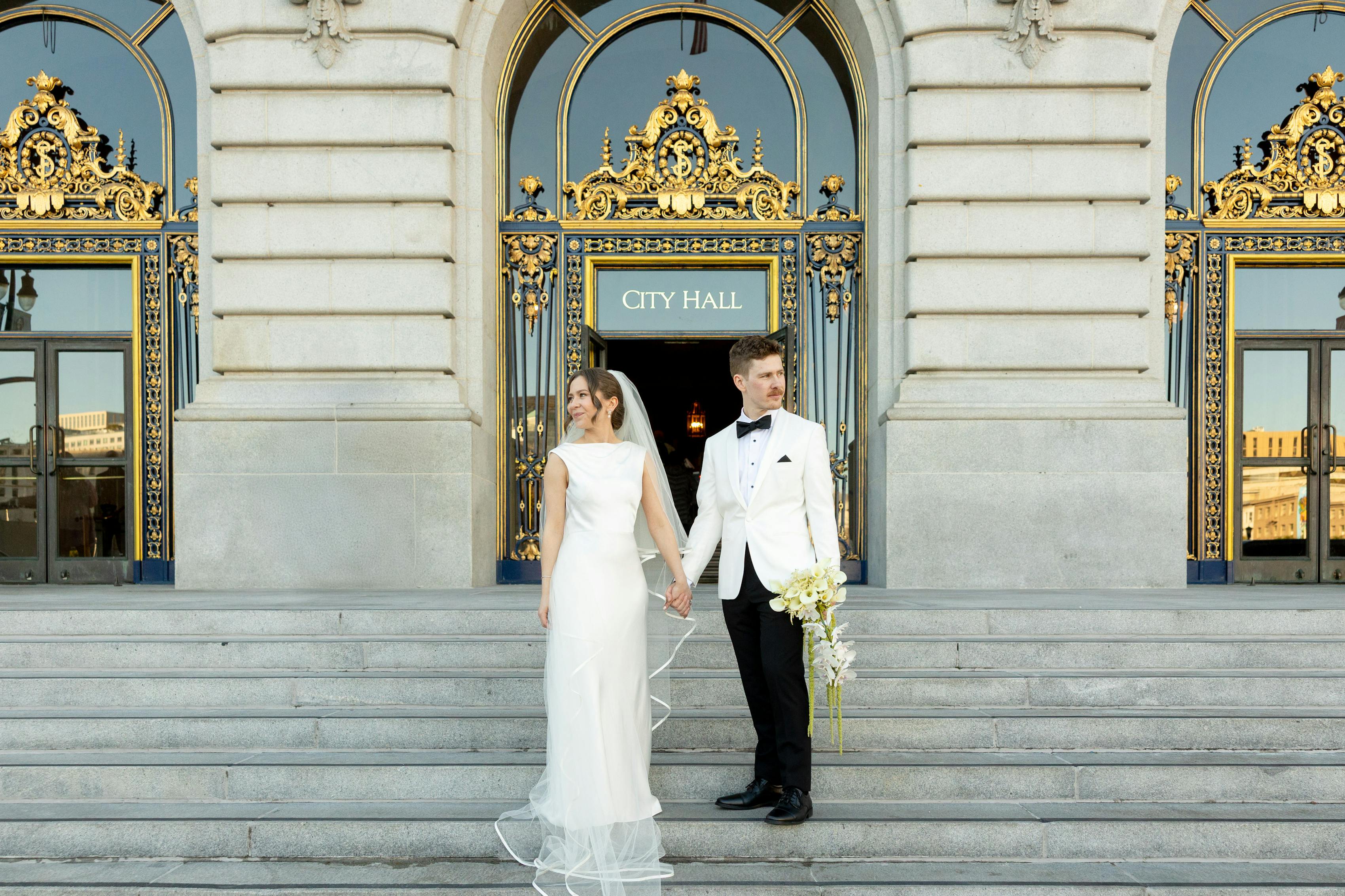 Bride and groom wearing formal city hall wedding outfits with gown and white tuxedo