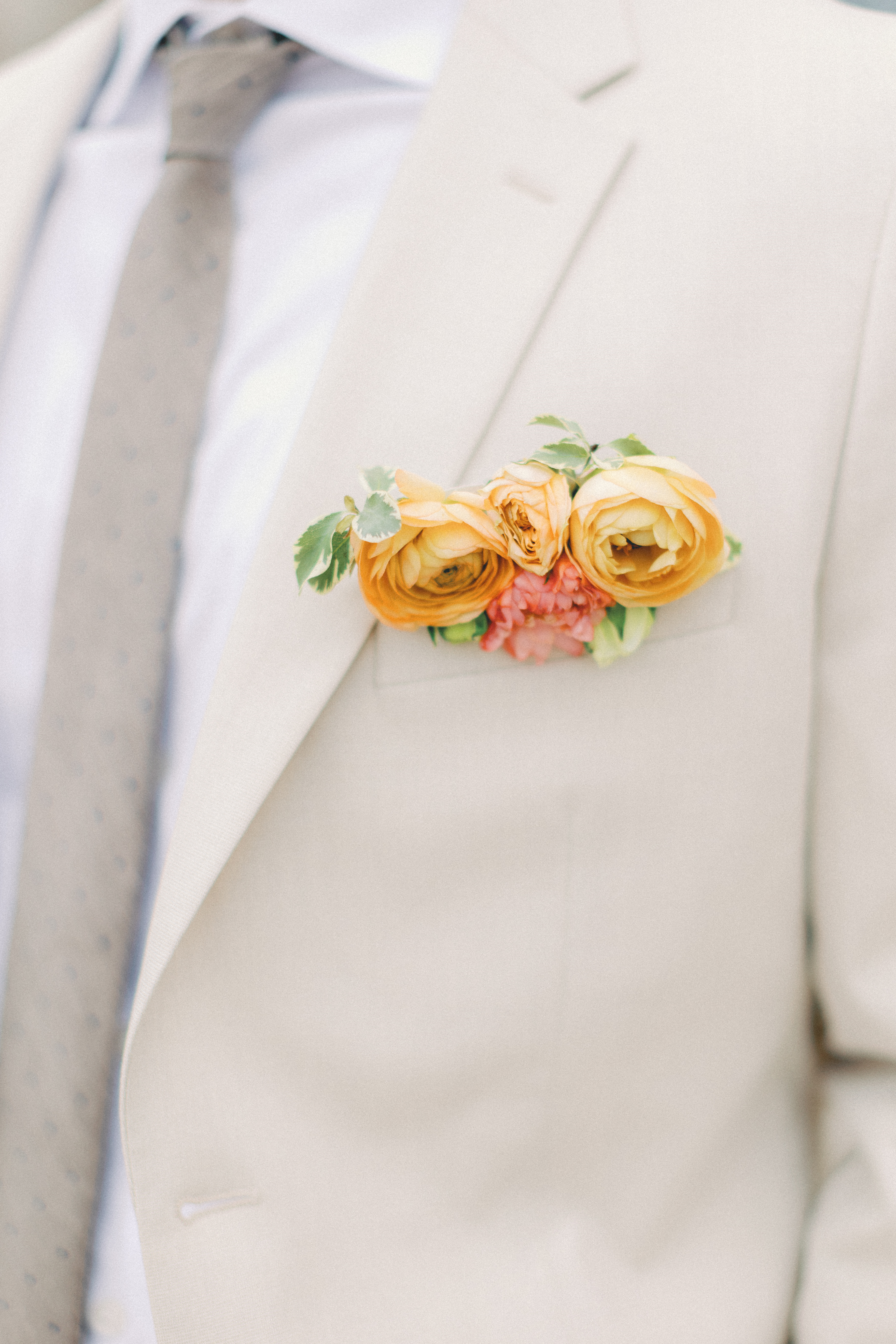 Light tan groom's suit with yellow, orange, sage, and island citrus floral pocket boutonnière