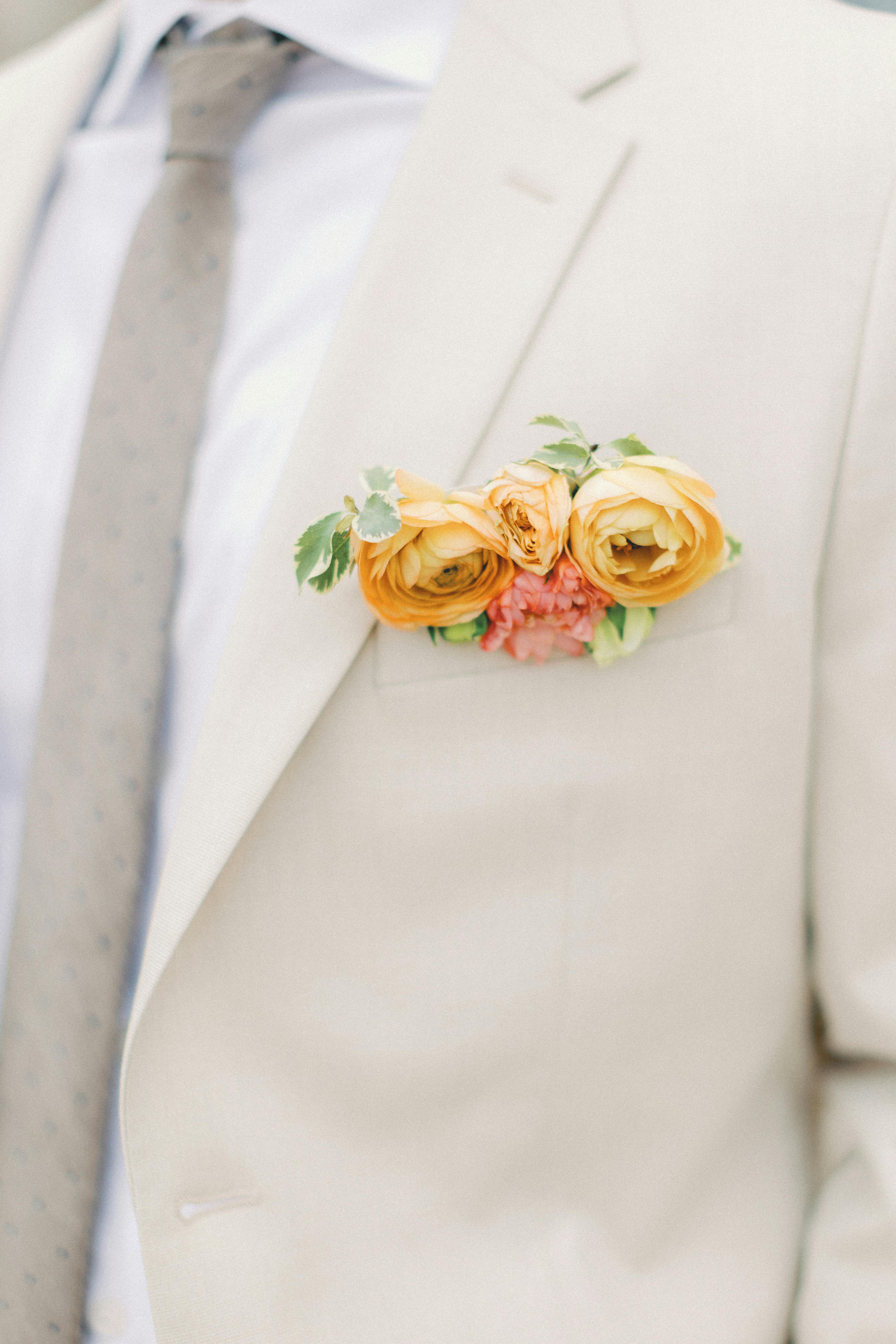 Light tan groom's suit with yellow, orange, sage, and island citrus floral pocket boutonnière