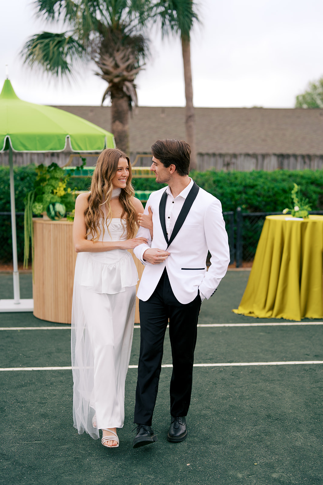 Bride and groom linking arms in front of lemon and lime wedding decor on tennis court
