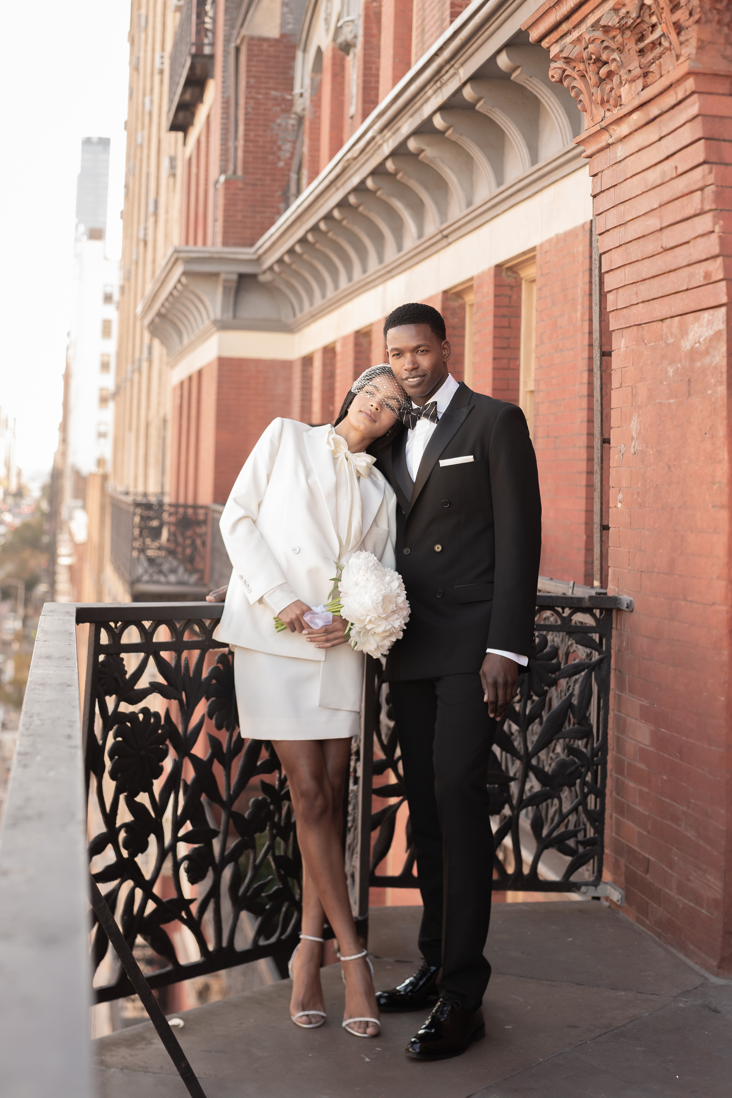 Newlyweds on NYC balcony wearing courthouse outfits with bridal suit and skirt and tuxedo
