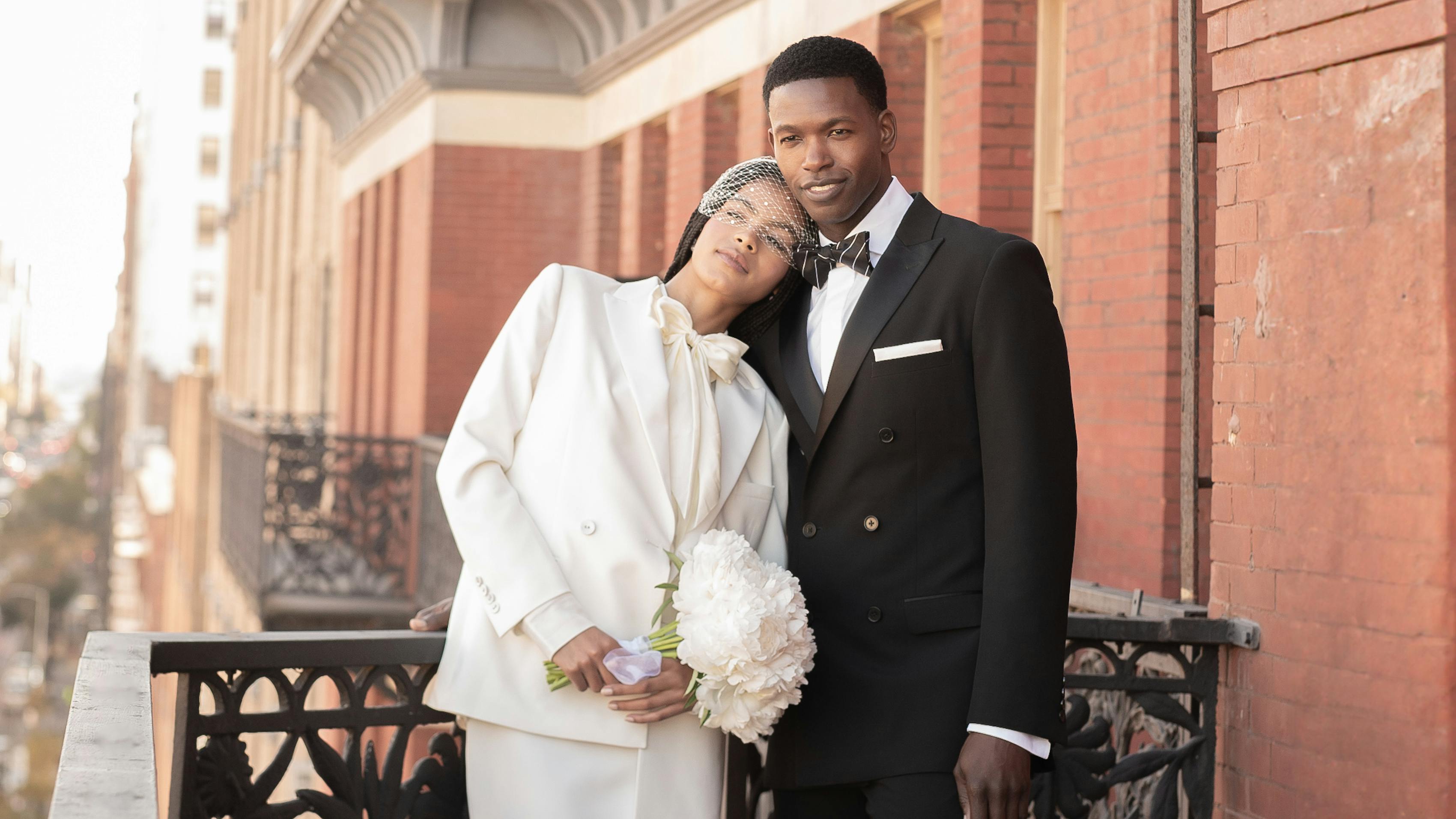 Newlyweds on NYC balcony wearing courthouse outfits with bridal suit and skirt and tuxedo