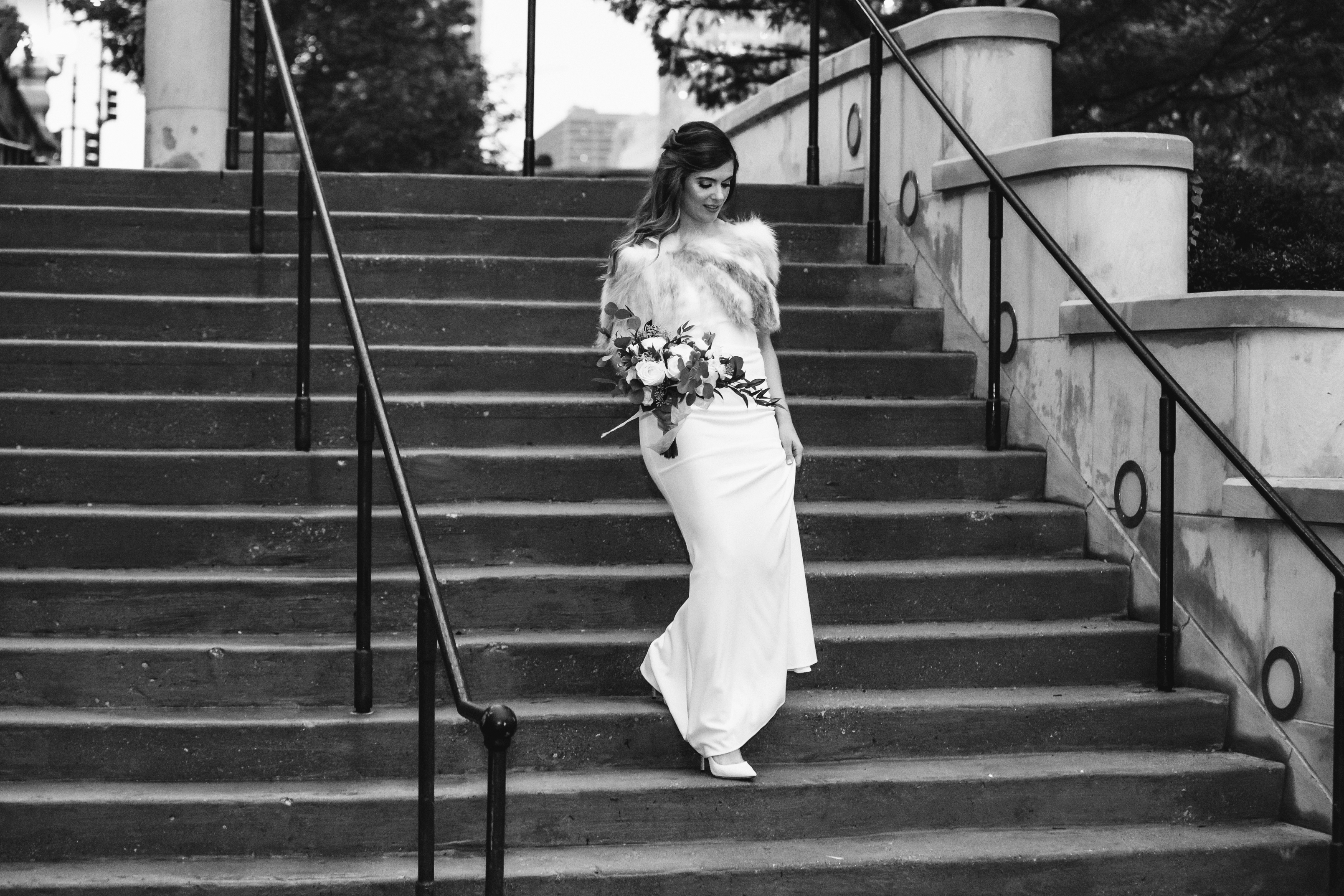 Bride walking down courthouse steps in long simple dress with fur shawl