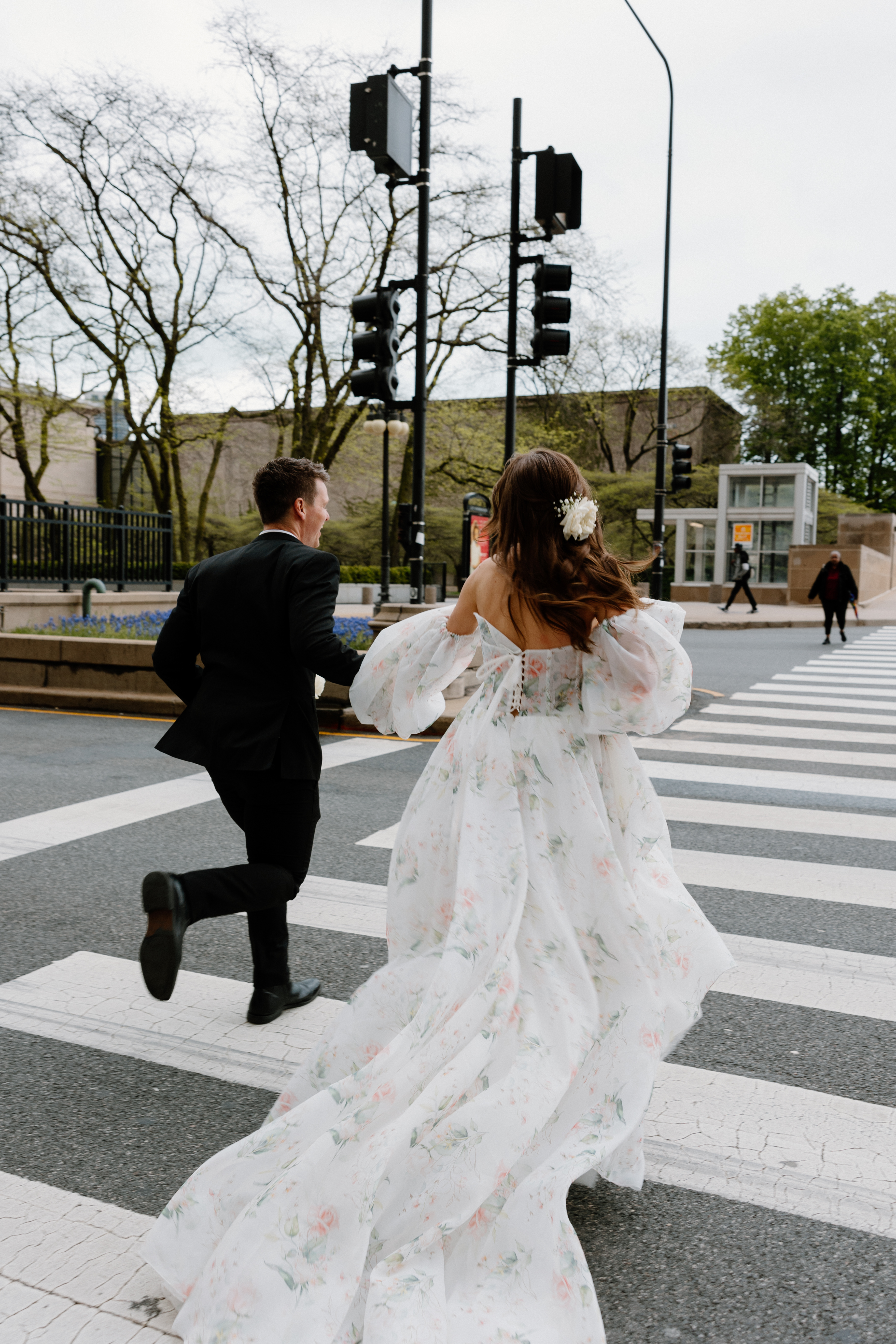 Bride and groom running across street in black suit and floral tulle gown