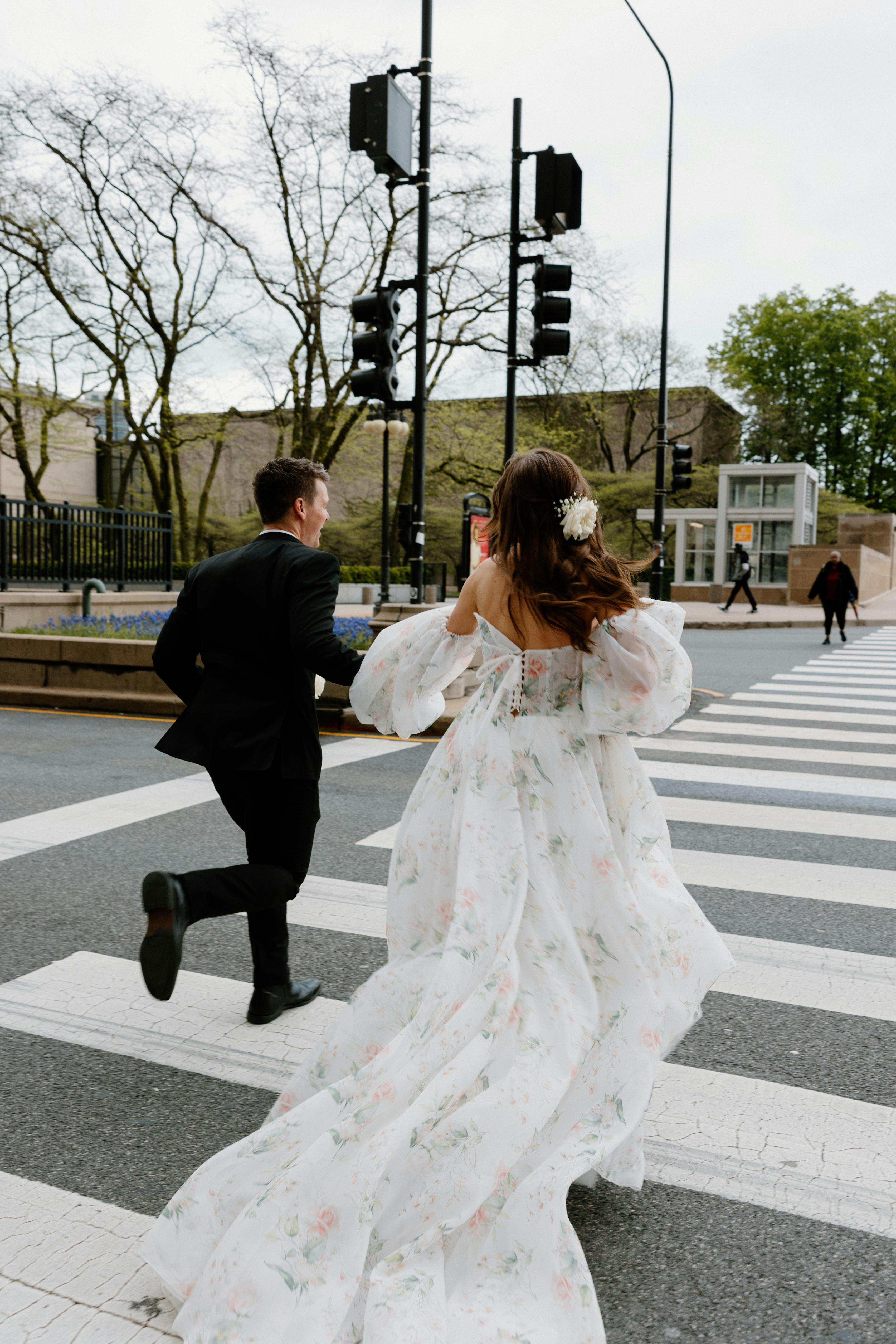 Bride and groom running across street in black suit and floral tulle gown