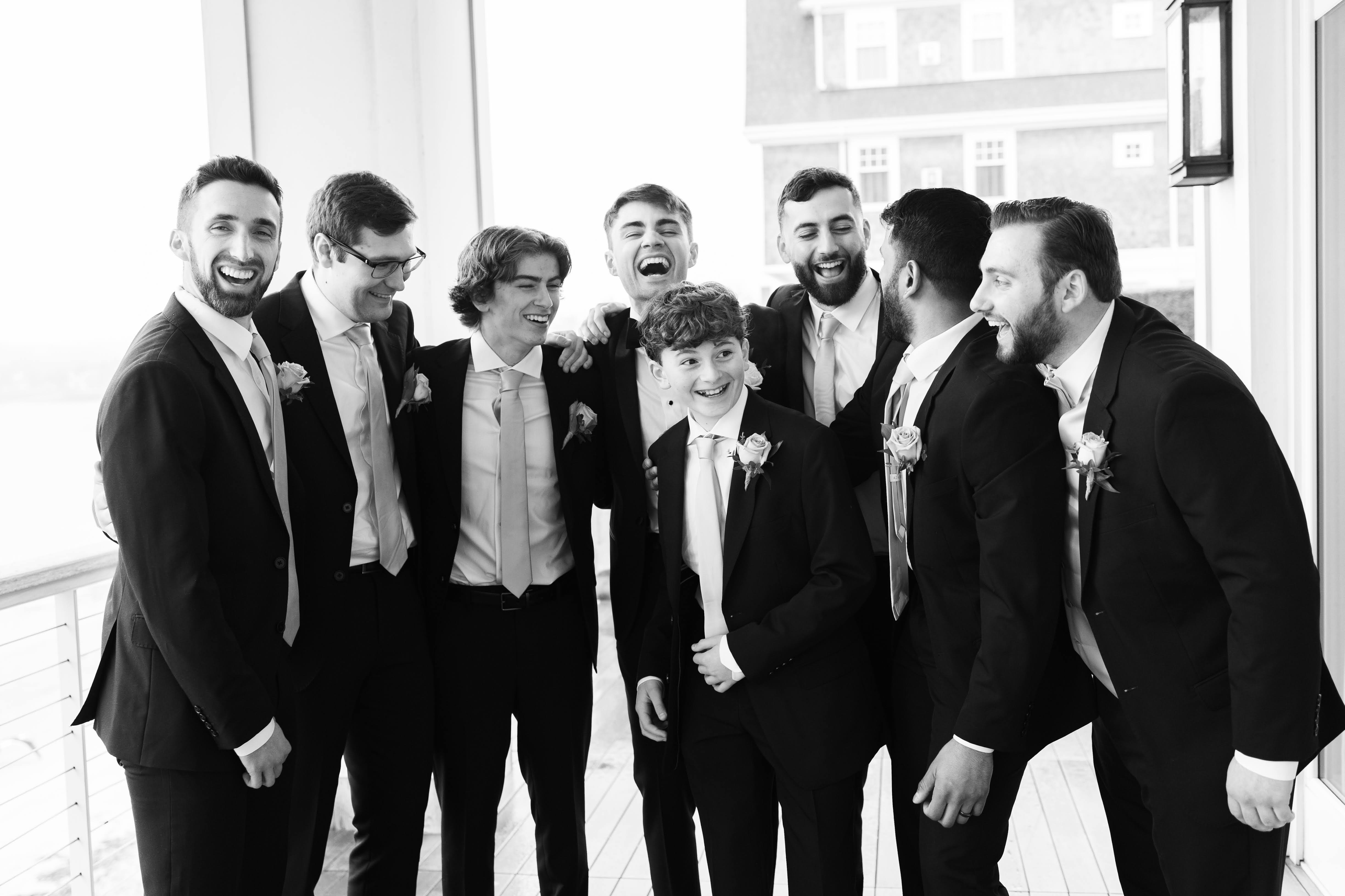 A black and white photo of the a groom and groomsmen laughing in a group at a wedding.