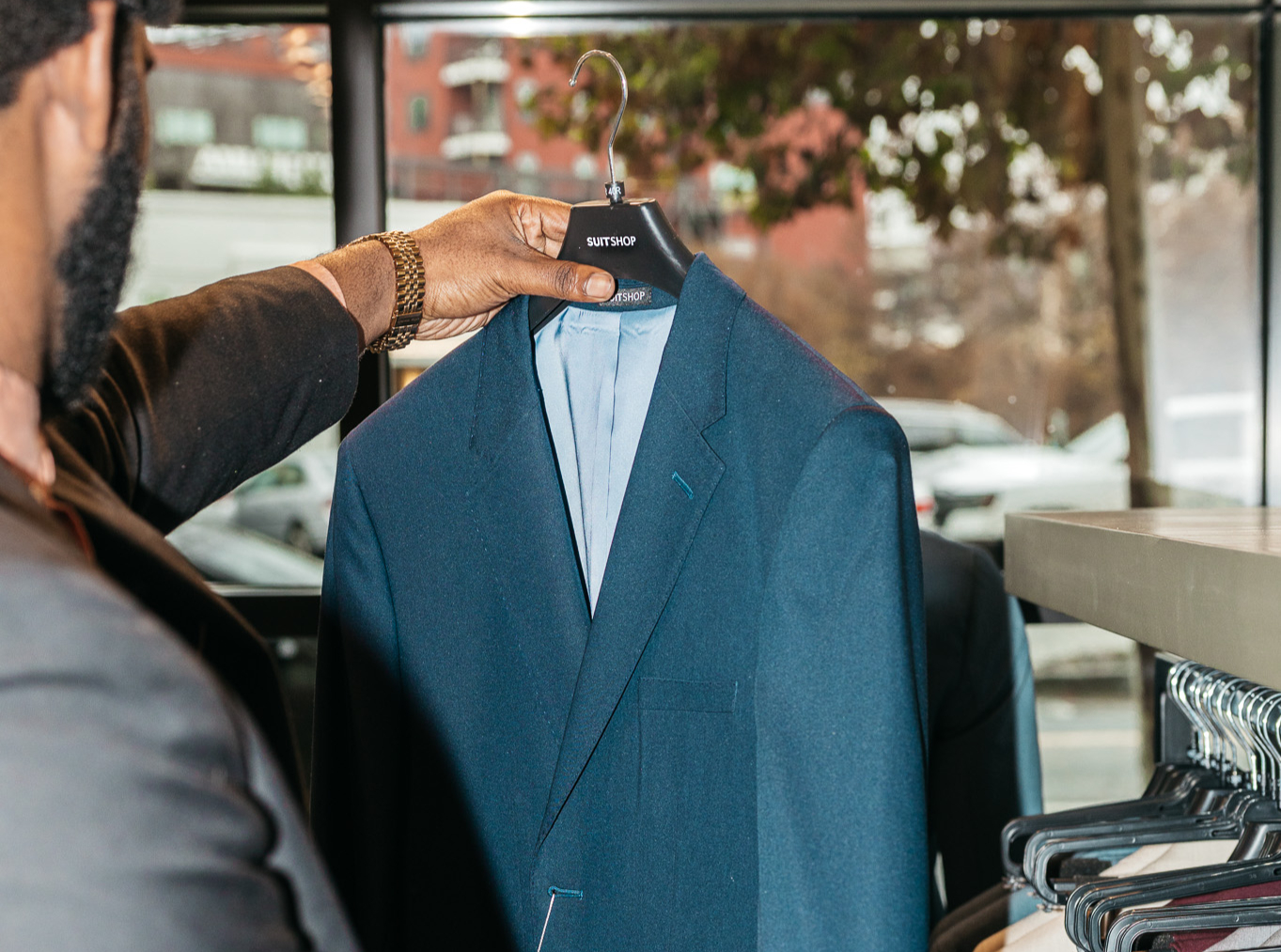 Man picking out a navy blue suit jacket on a hanger from a SuitShop showroom.