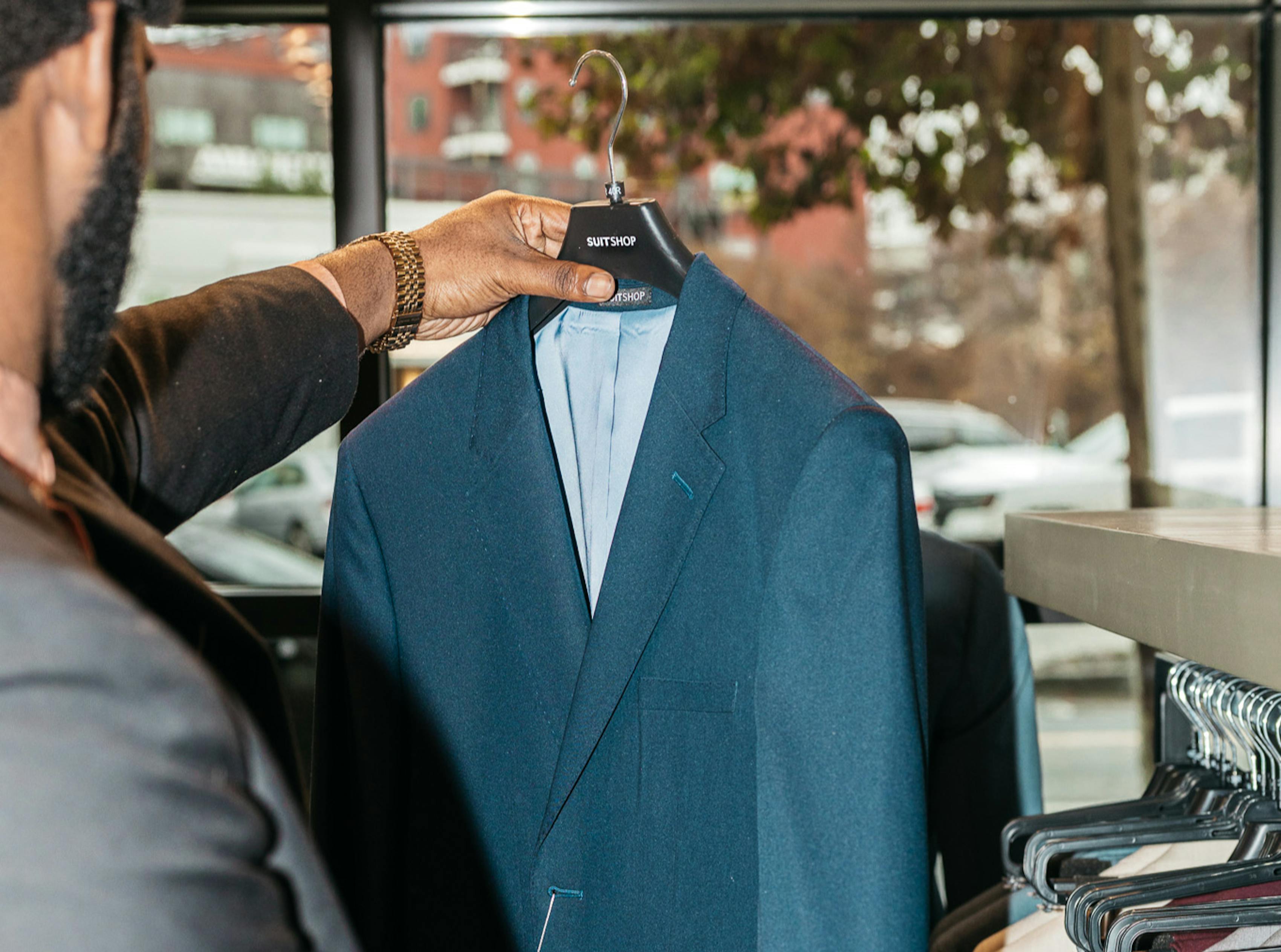 Man picking out a navy blue suit jacket on a hanger from a SuitShop showroom.