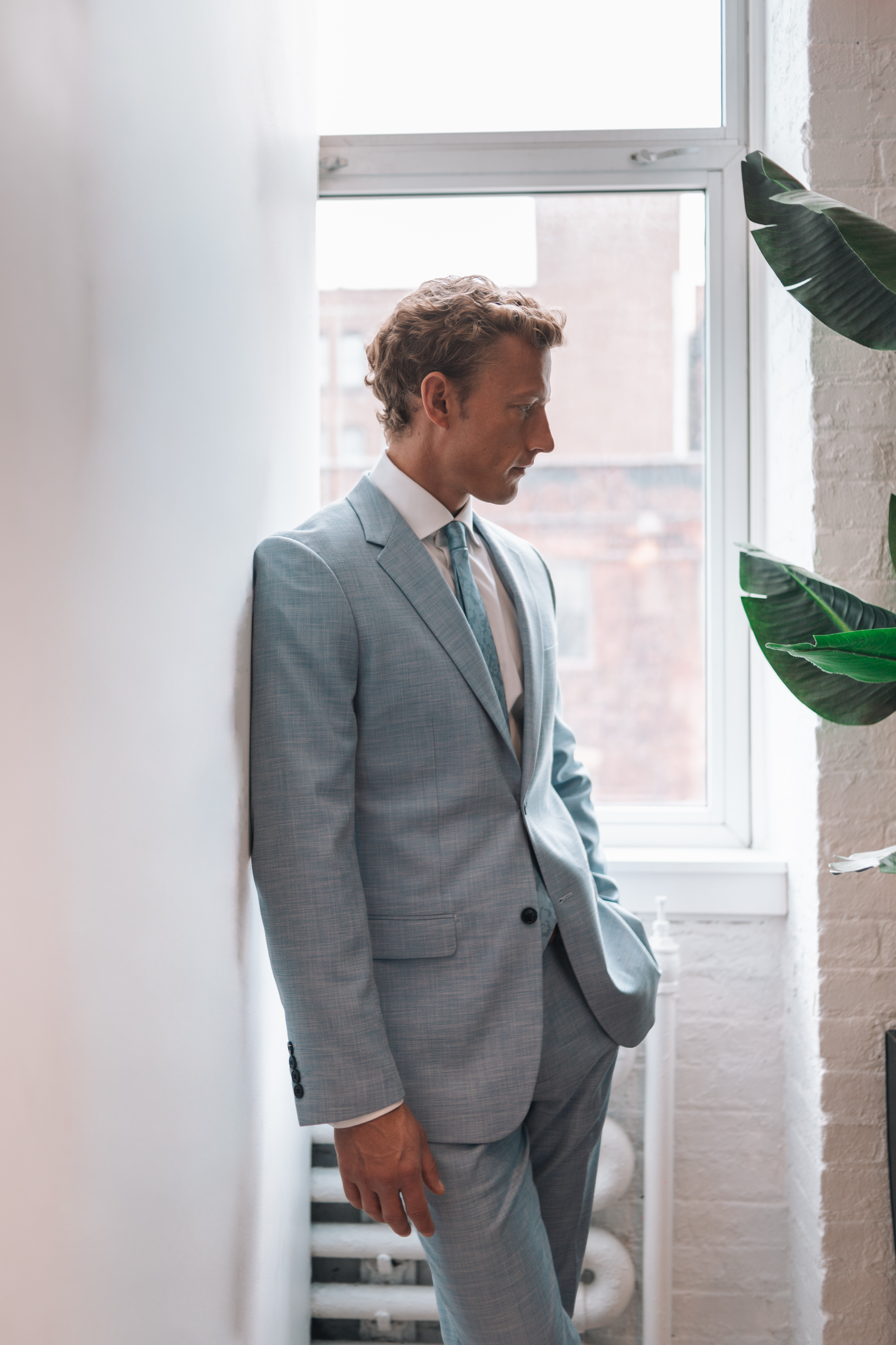 Man wearing light blue linen suit by tropical leaves for colorful wedding outfit