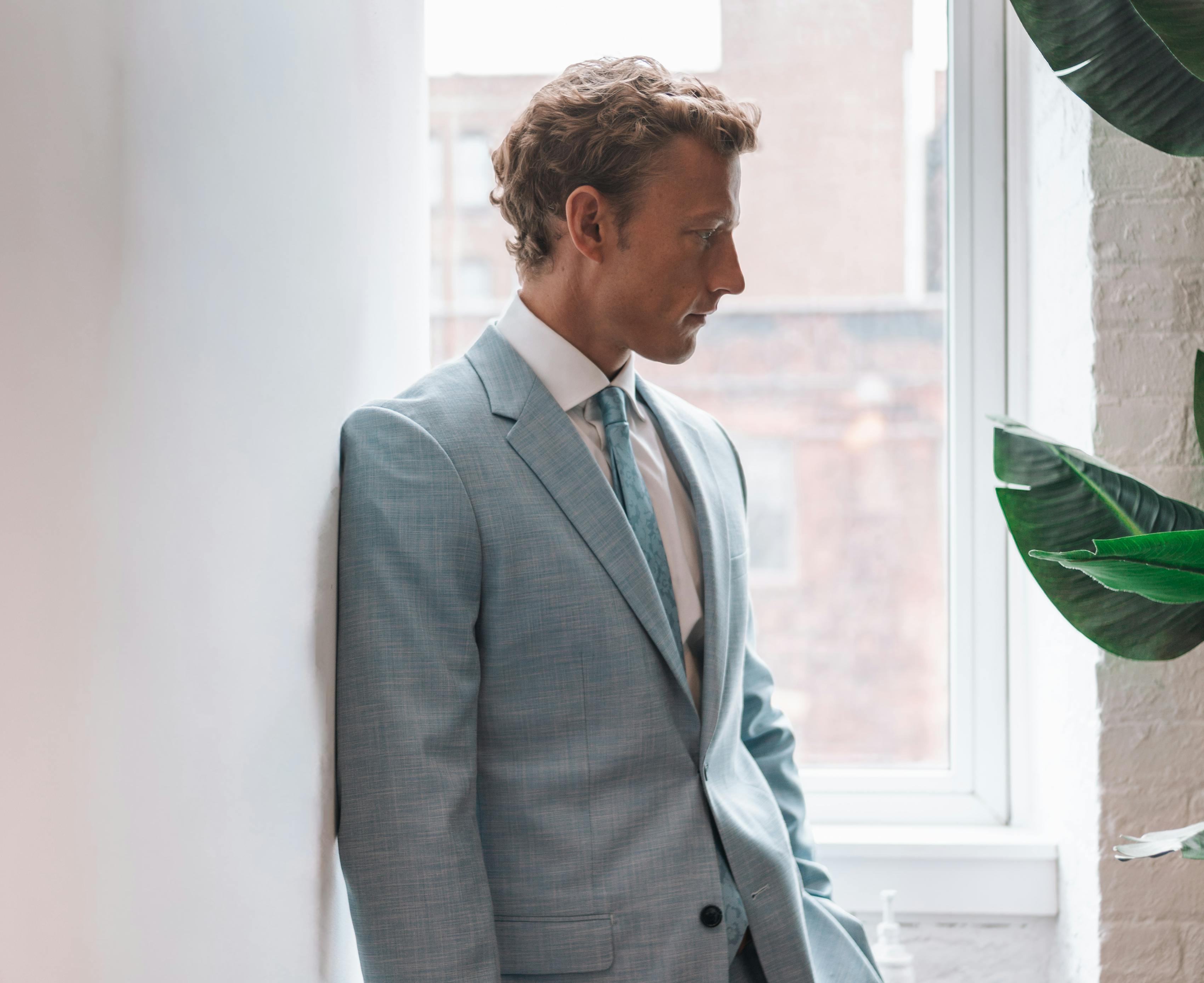 Man wearing light blue linen suit by tropical leaves for colorful wedding outfit