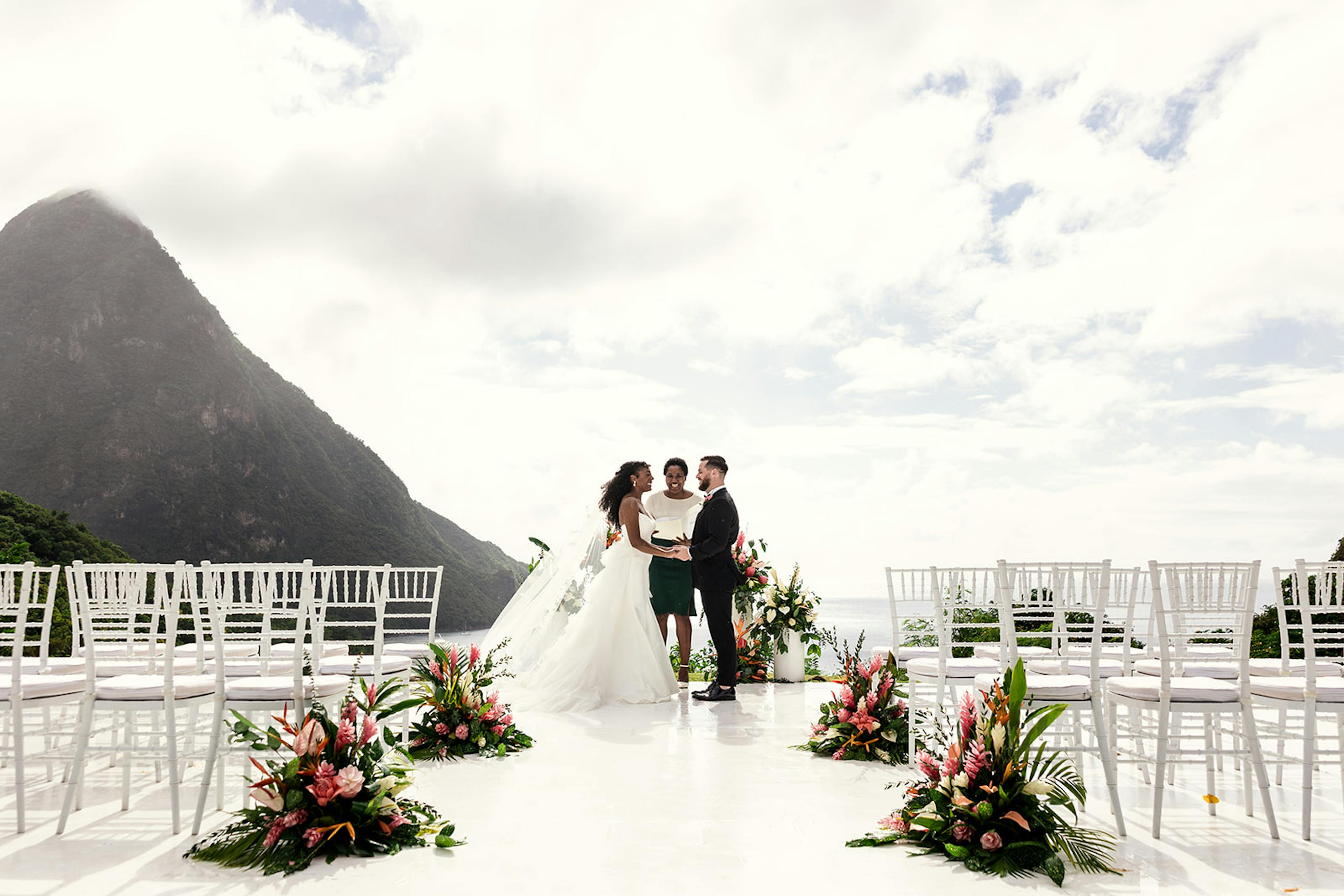 Couple at altar of sleep tropical island wedding venue in front of mountain and ocean