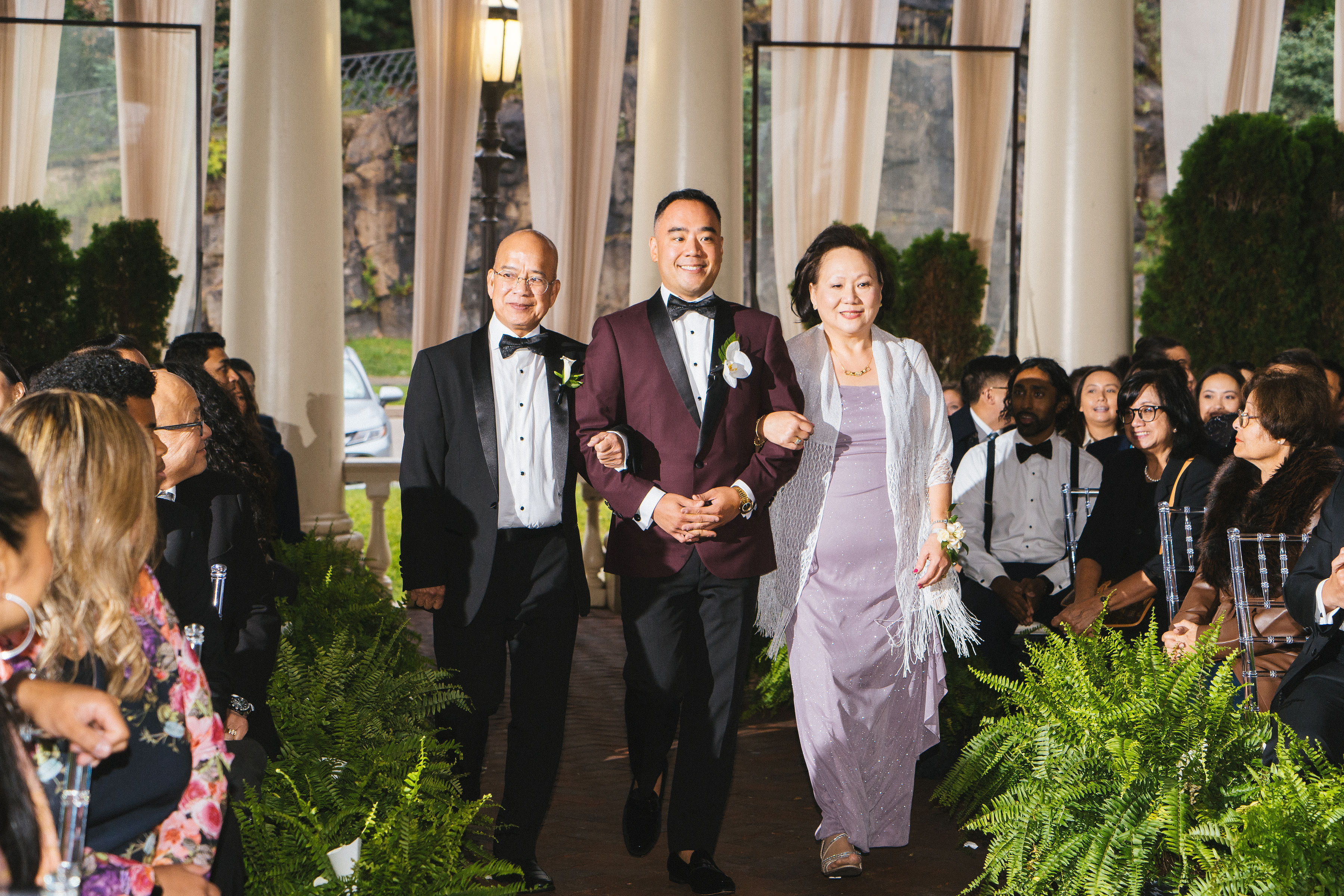 A groom walking down the aisle, escorted by his mother and father.