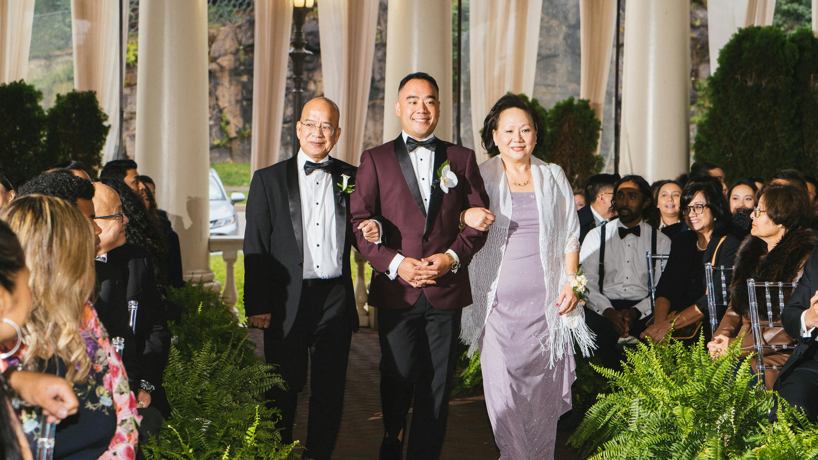 A groom walking down the aisle, escorted by his mother and father.