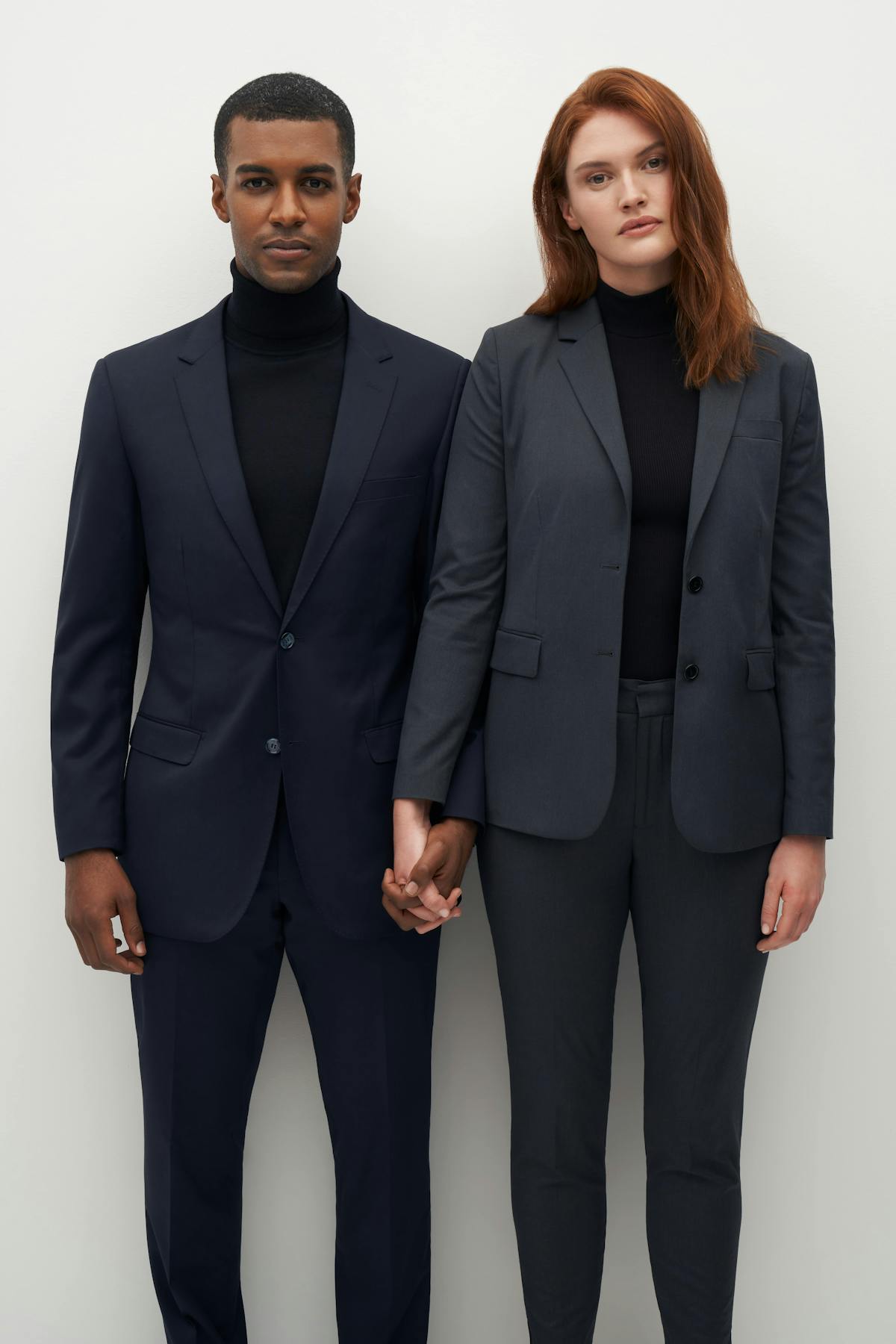 Matching men's and women's suits in dark grey with a turtleneck for professional outfits.