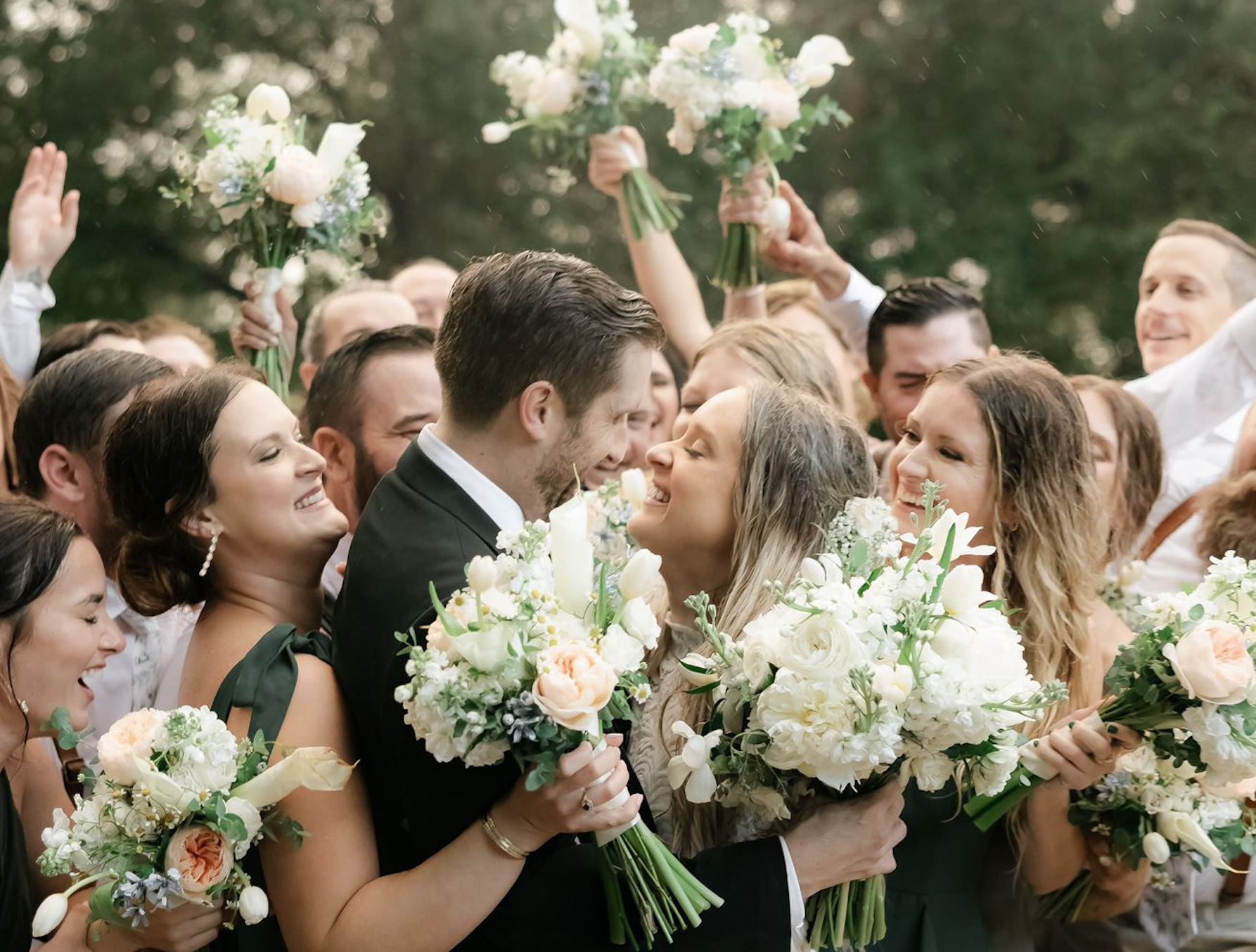 A bride and groom look lovingly at one another as they're surrounded by wedding guests. Most of the wedding guesrs are holding a flower bouquet, so it appears to be a sea of people and flowers surrounding the newlyweds.