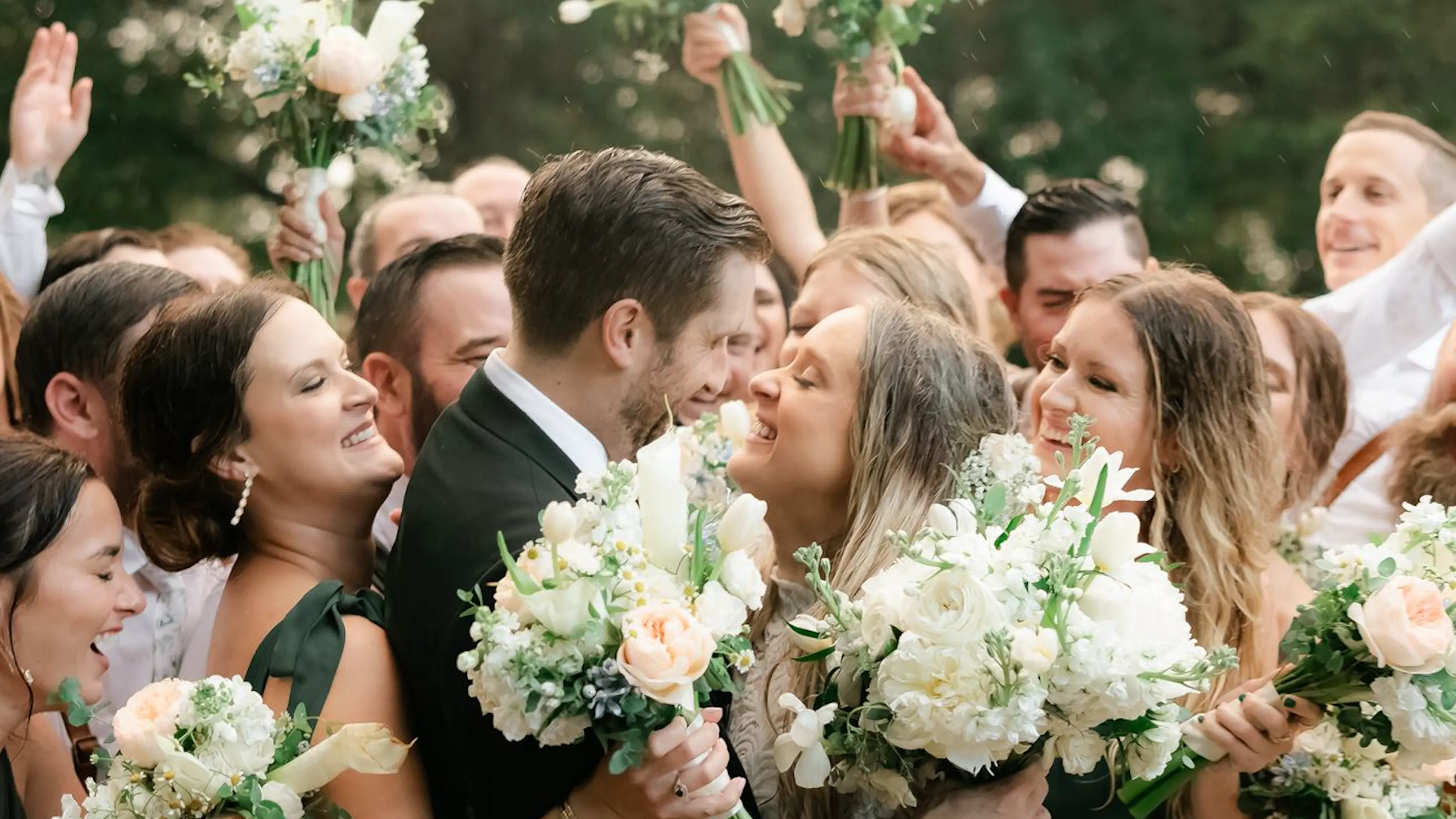 A bride and groom look lovingly at one another as they're surrounded by wedding guests. Most of the wedding guesrs are holding a flower bouquet, so it appears to be a sea of people and flowers surrounding the newlyweds.