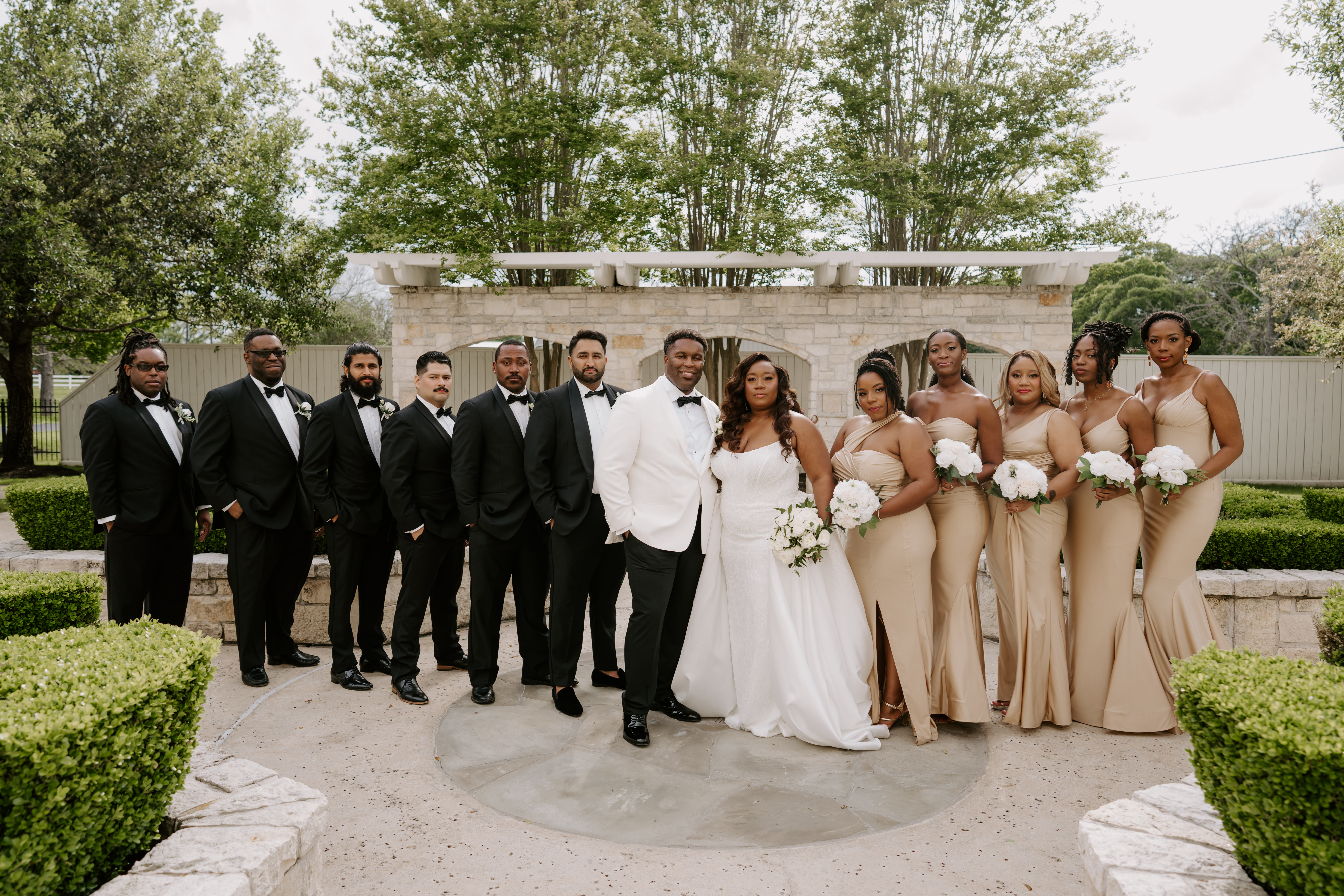The entire wedding party stands in a courtyard. The groom's side is to the left and the bride's side is to the right.
