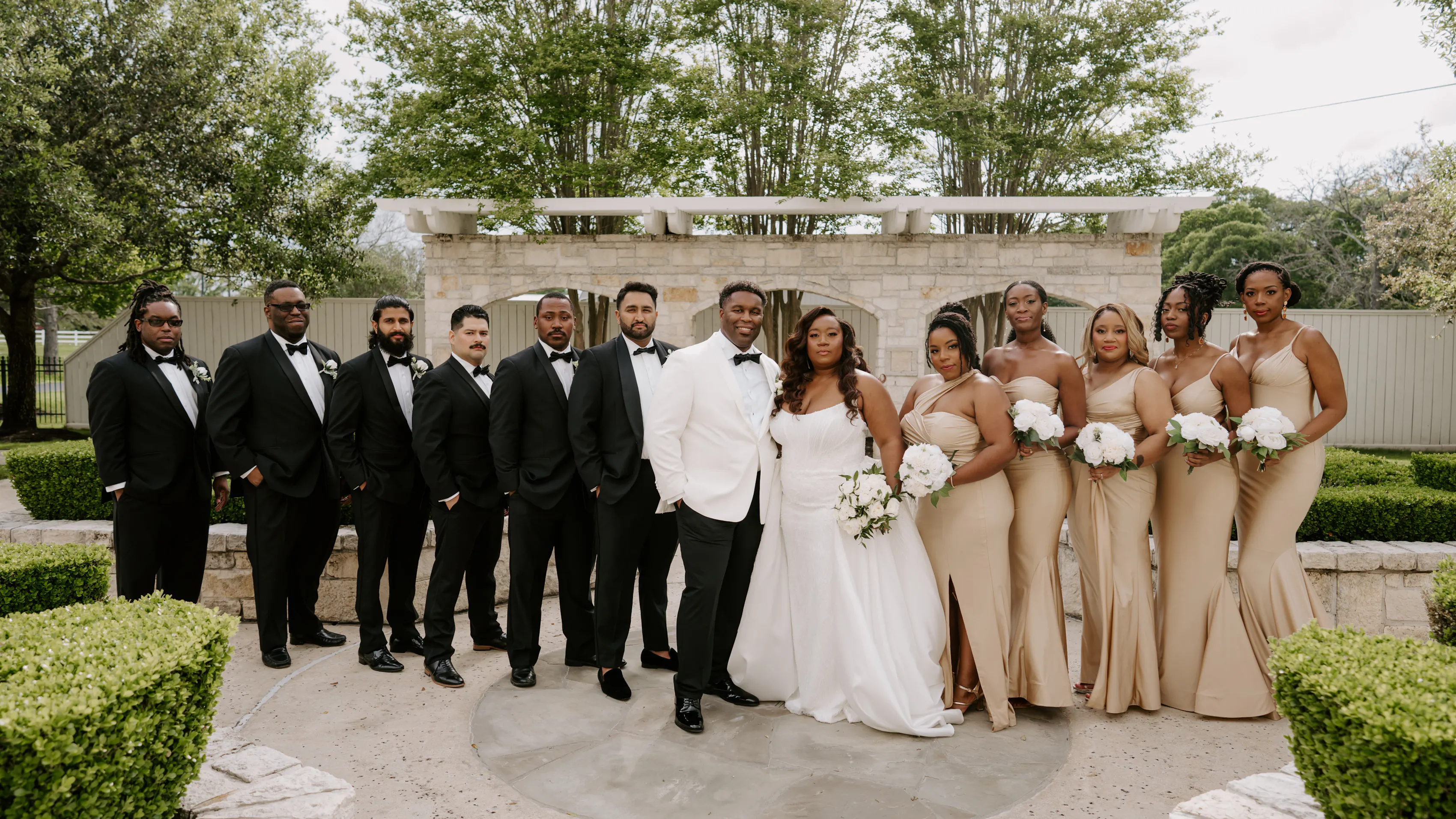 The entire wedding party stands in a courtyard. The groom's side is to the left and the bride's side is to the right.