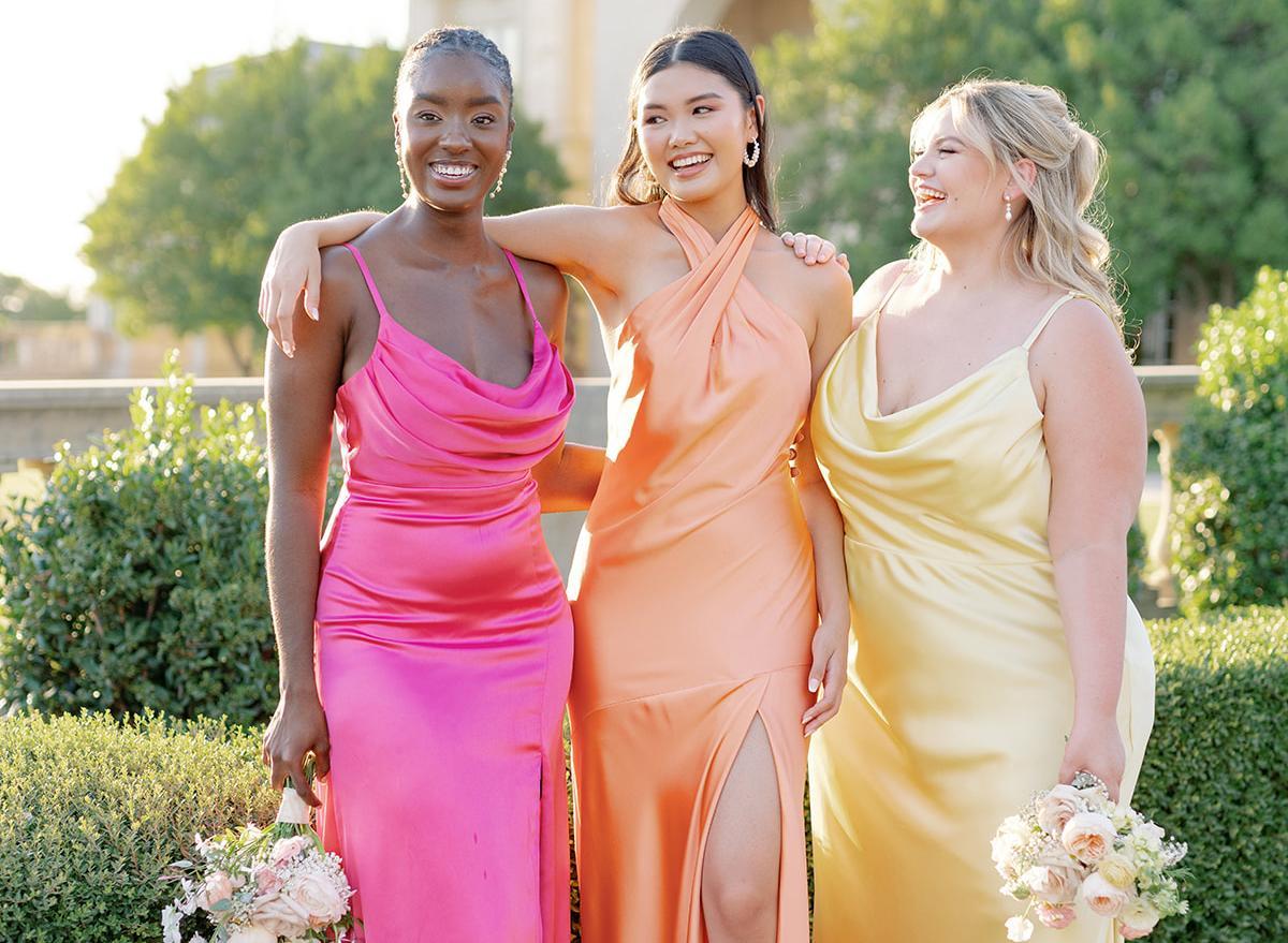 A group of three bridesmaids pose for a photo: lthe eft woman is in pink, the middle is in orange, and the right is in yellow.