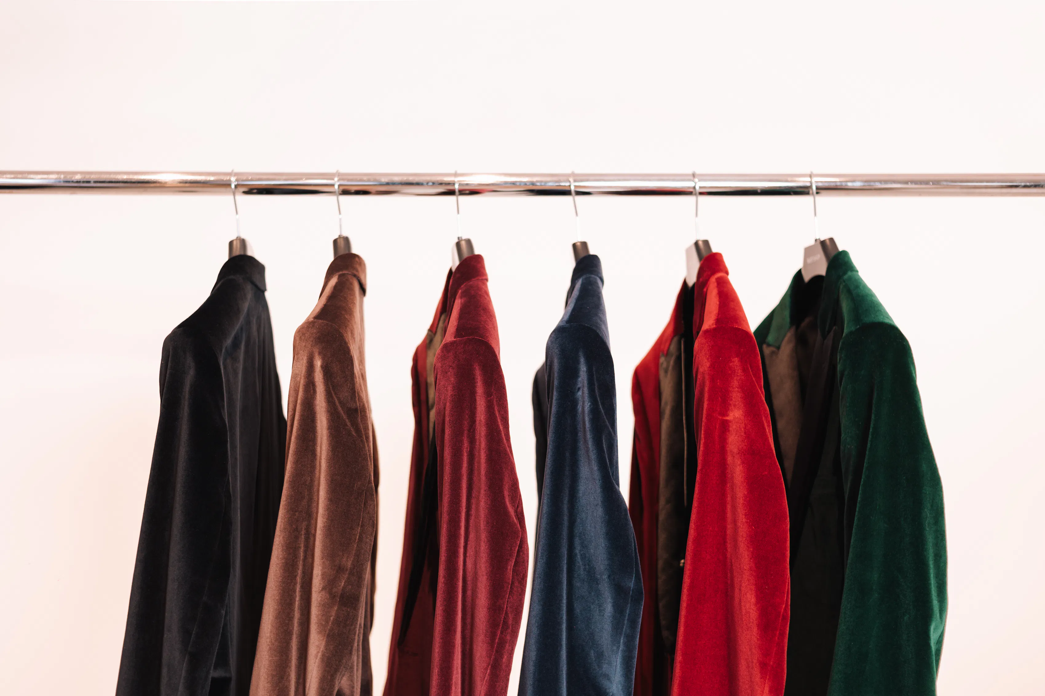 6 velvet suits in various colors hanging on a rack.