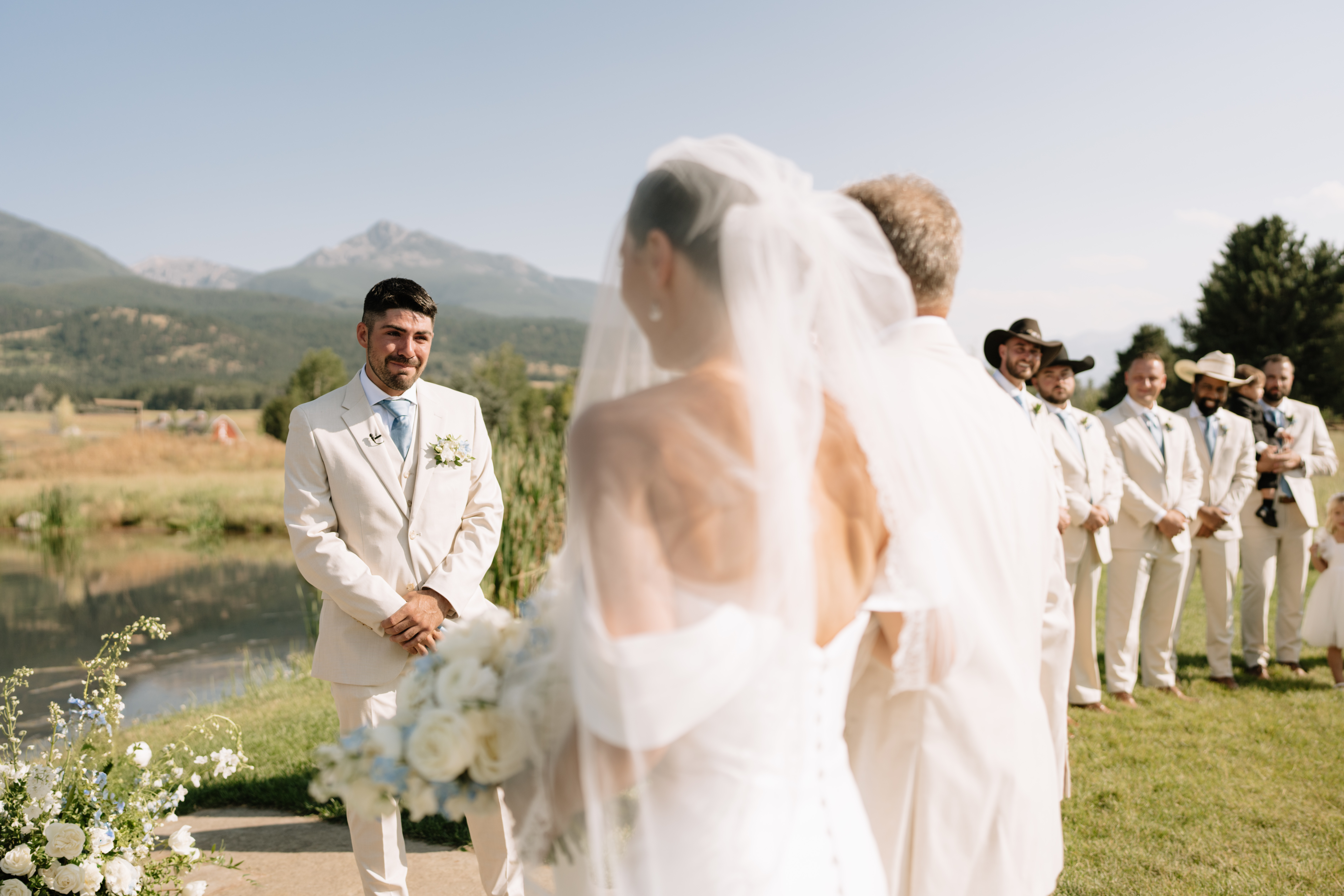 A woman, back to the camera, stands across from her fiancee at their outdoor wedding. 