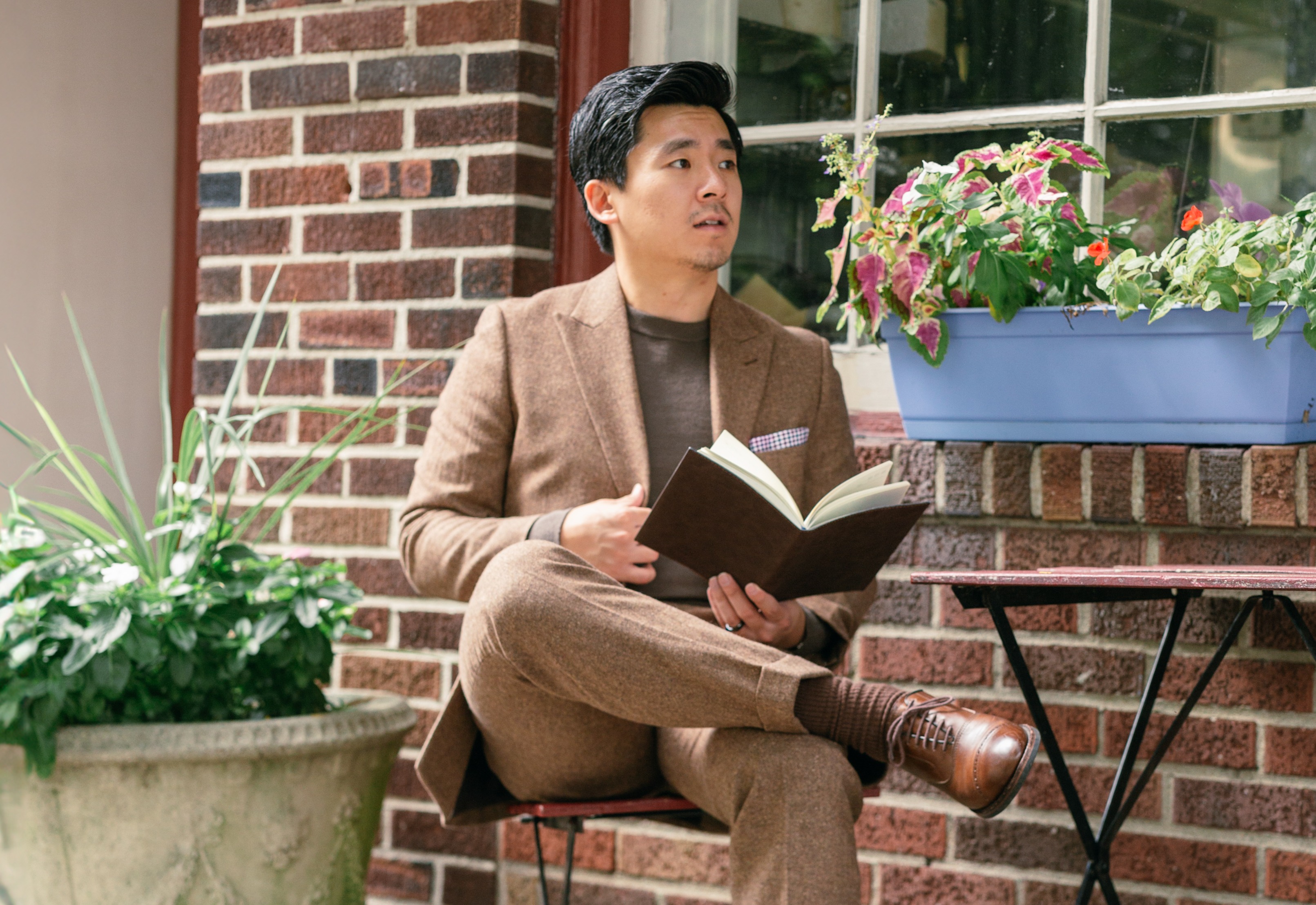 A man in dressy casual sitting at an outdoor cafe table, reading a book.