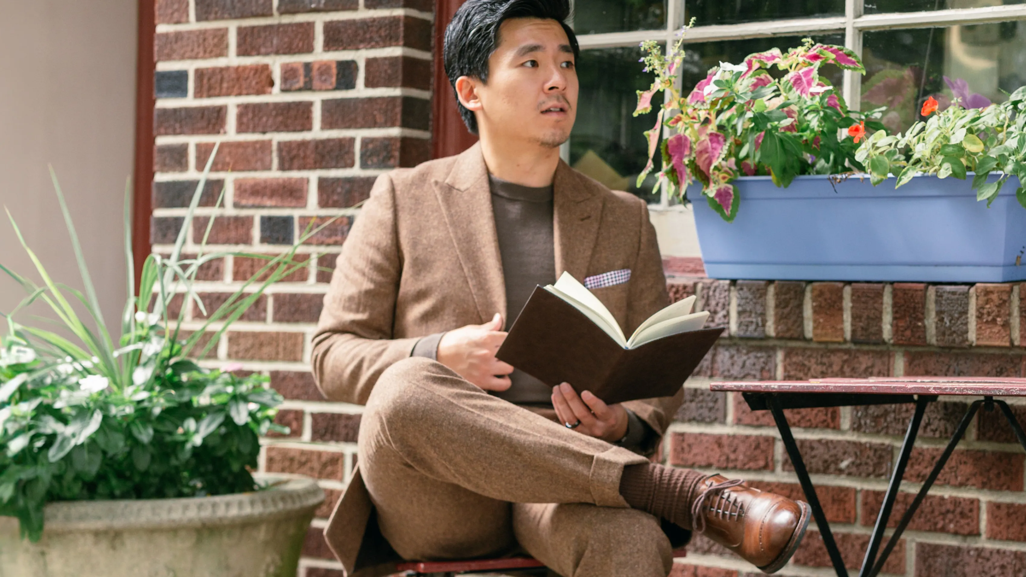 A man in dressy casual sitting at an outdoor cafe table, reading a book.
