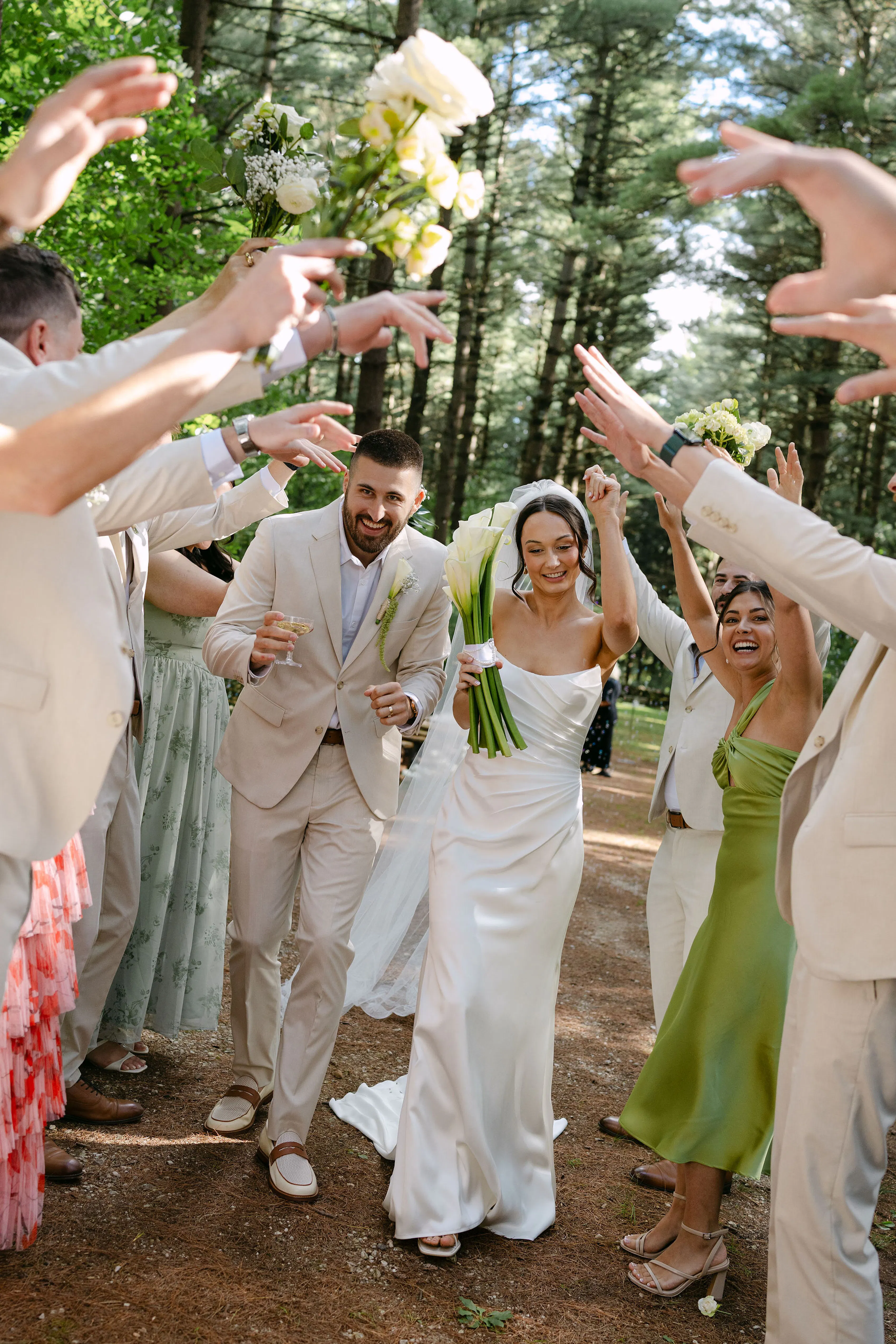 Bride and groom walking through colorful bridal party's hands at wedding in the woods