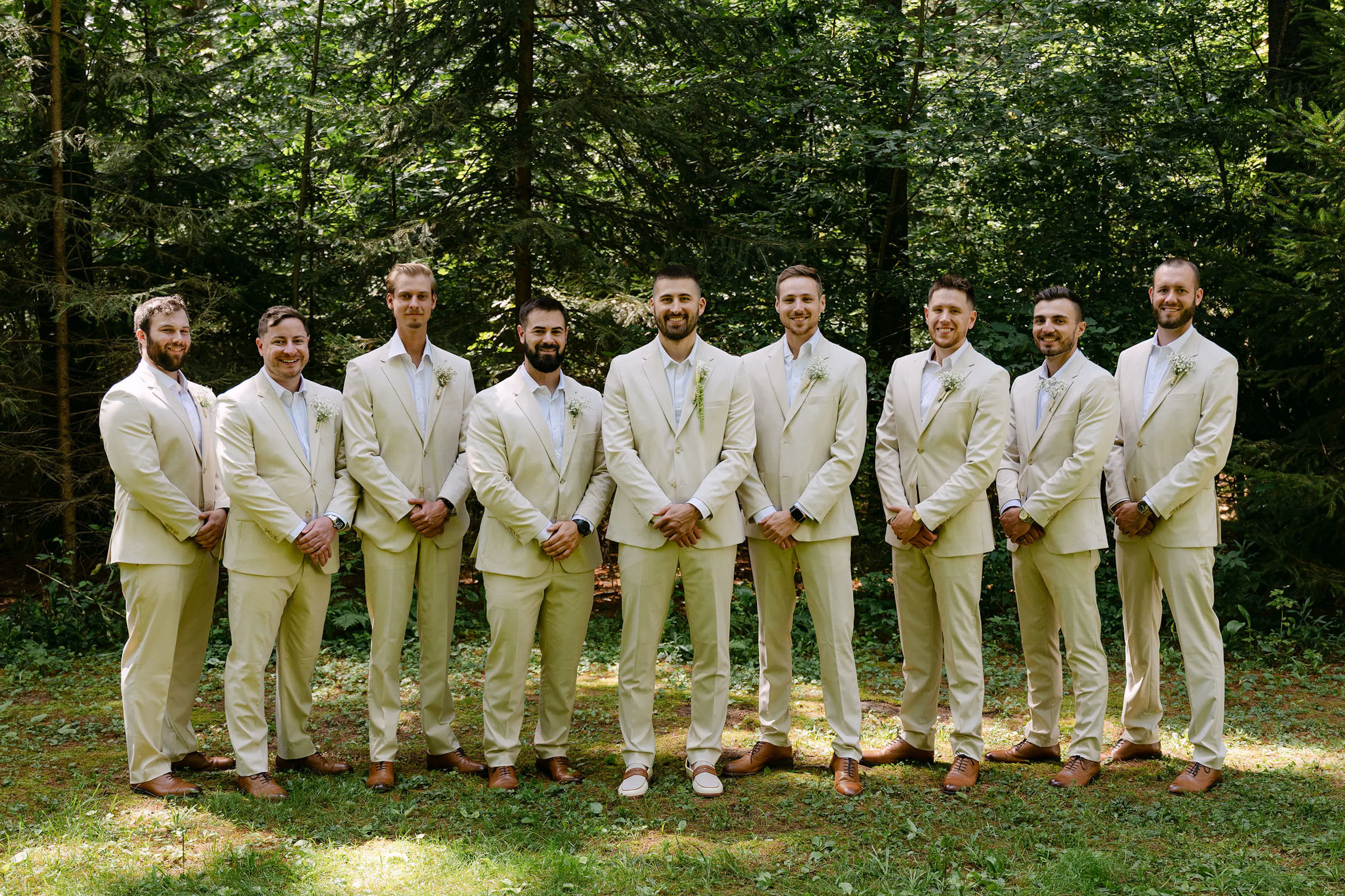 Tan suit groomsmen with no ties and brown shoes at outdoor rustic wedding