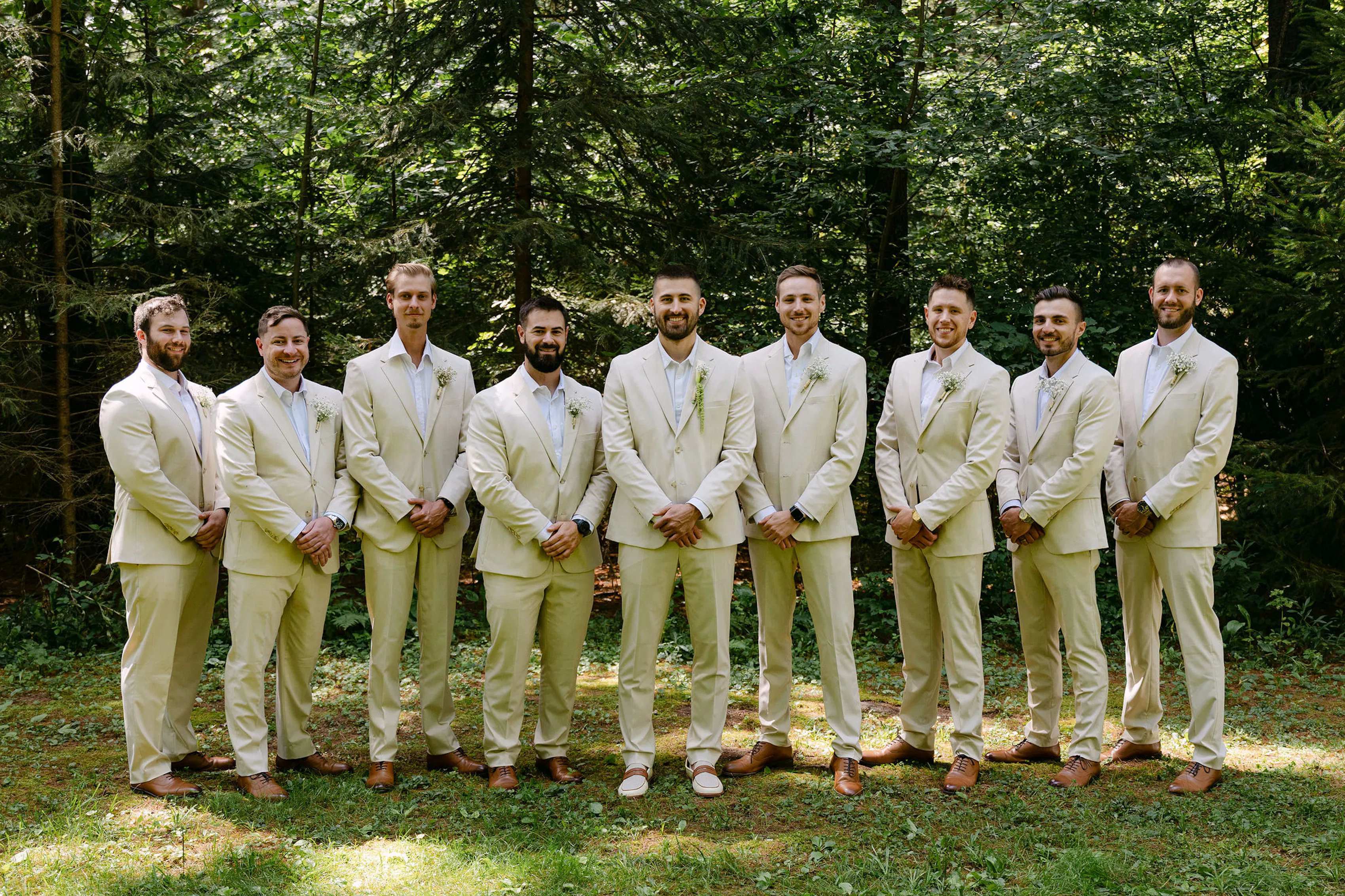 Tan suit groomsmen with no ties and brown shoes at outdoor rustic wedding