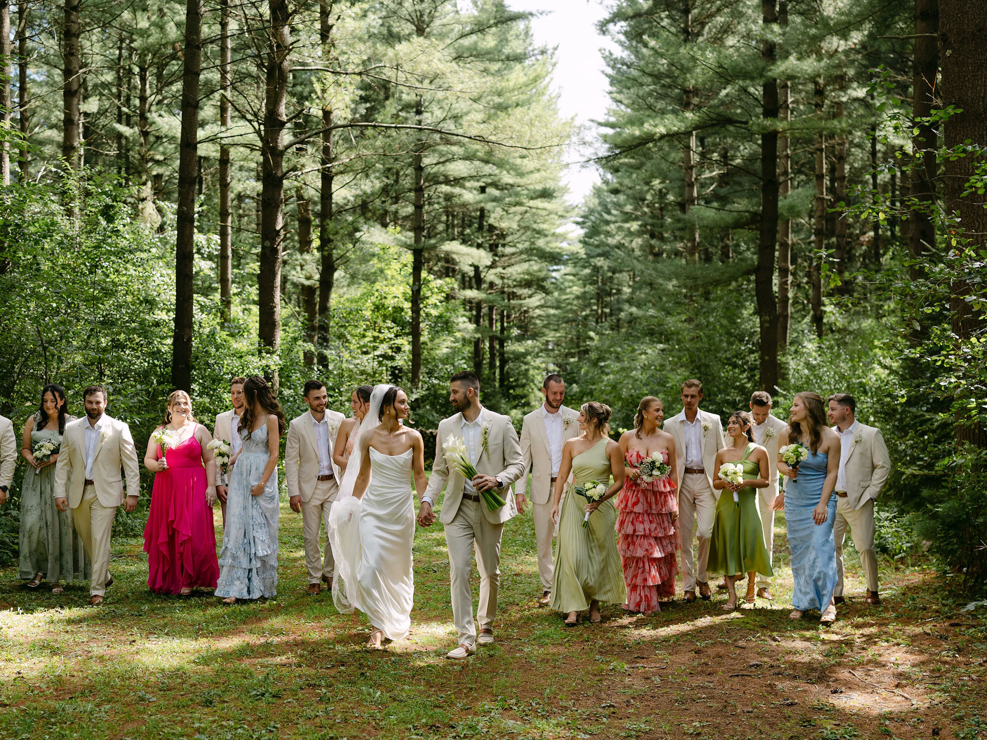 Bridal party walking through woods in colorful mix and match bridesmaid dresses and tan groomsmen suits