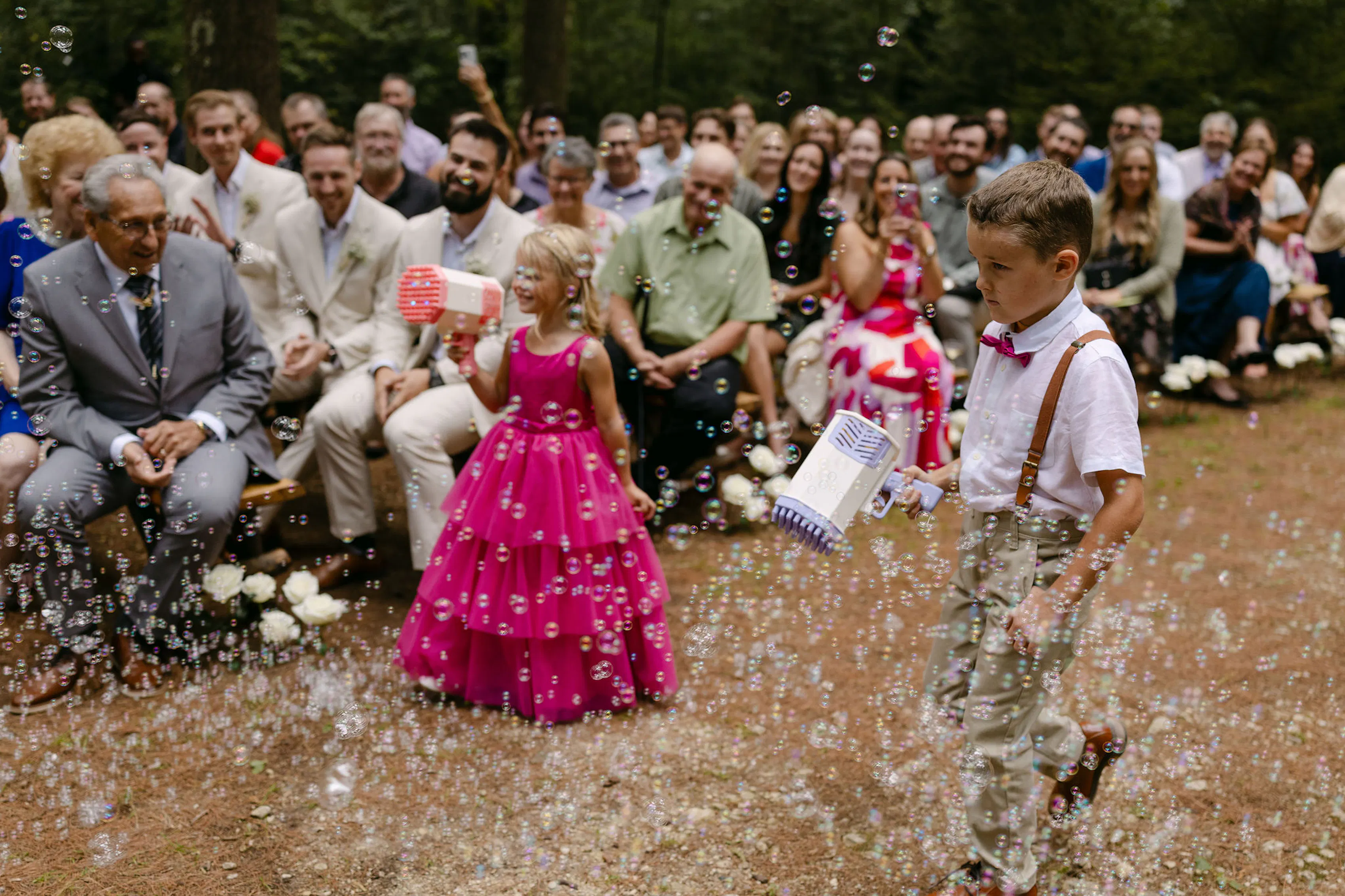 Ring bearer and flower girl blowing bubbles during wedding ceremony
