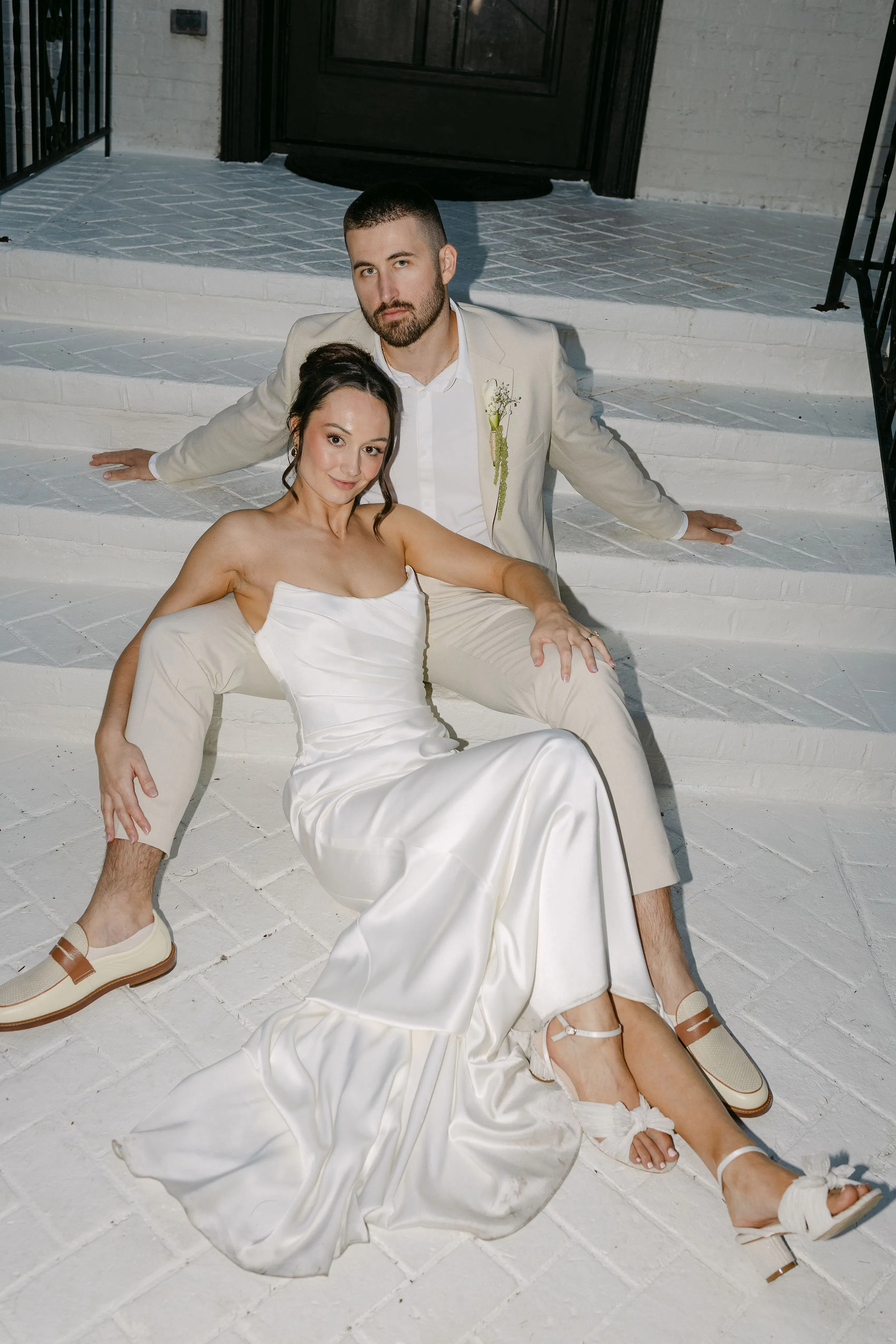 Bride in satin strapless gown and groom in casual tan wedding suit posing on stairs