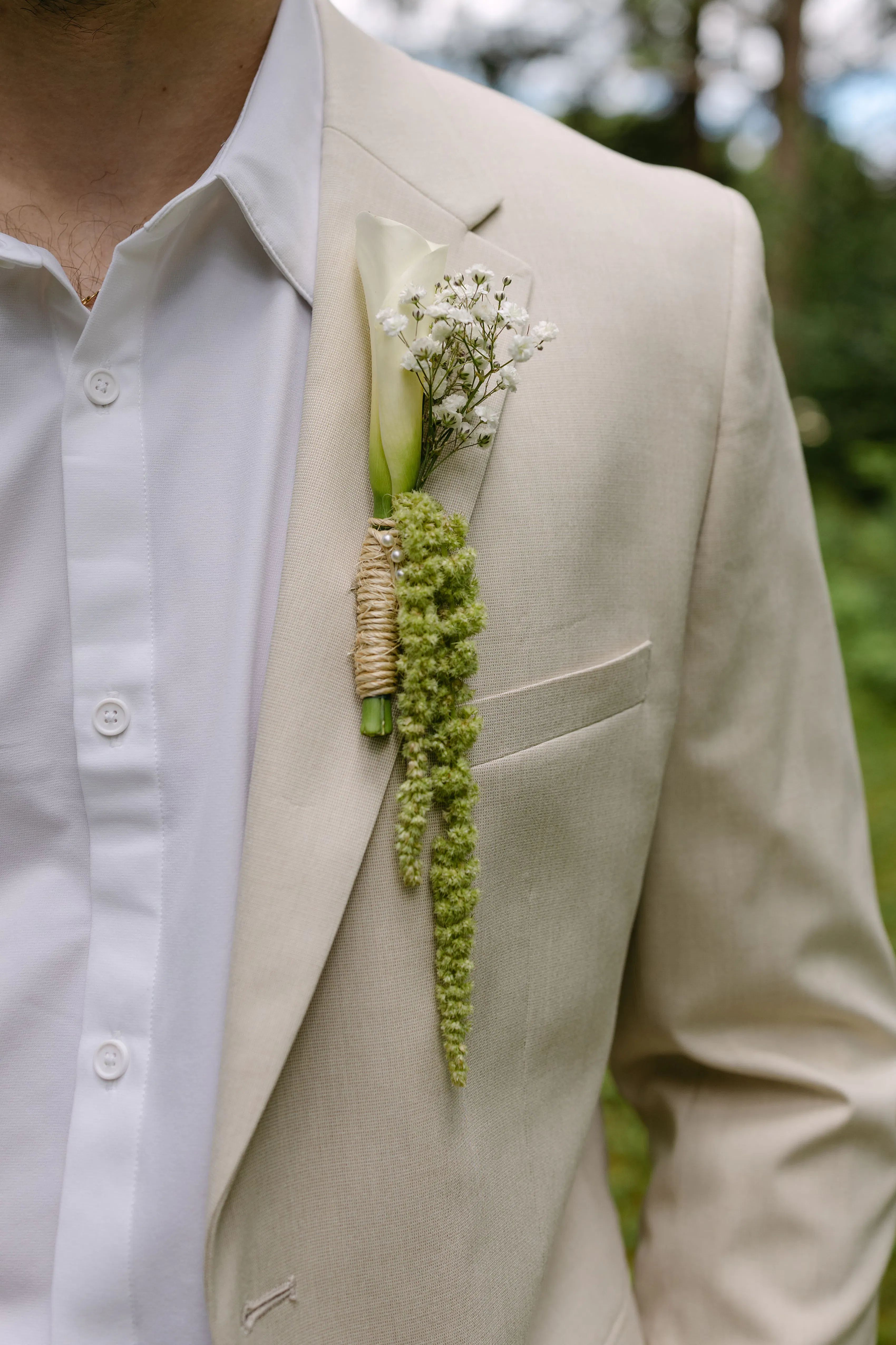 Groom's boutonniere with simple white calla lily and whimsical green hanging florals