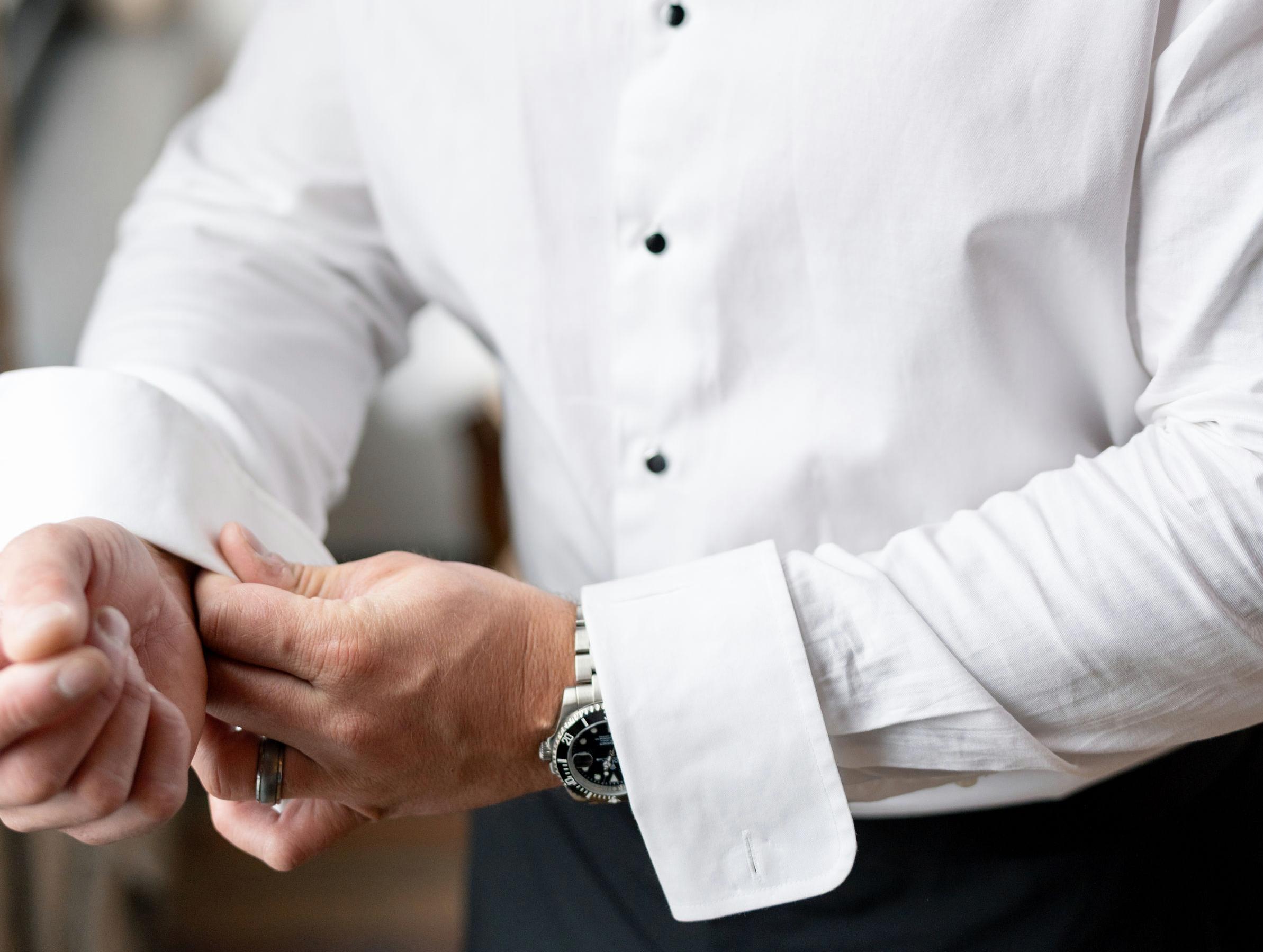 Close-up of a man buttoning the cuffs of his dress shirt.
