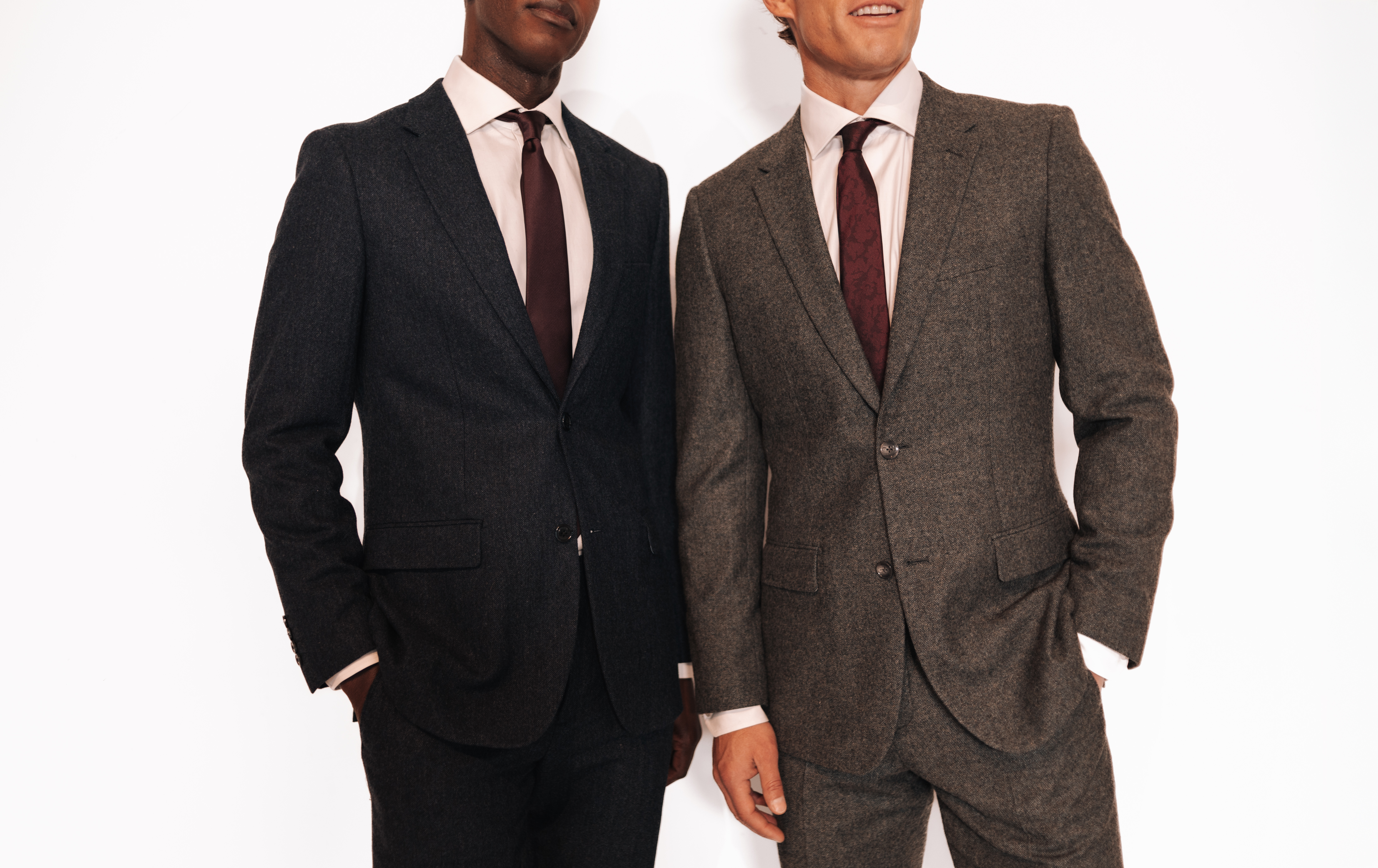 Two men, with their faces cropped, stand in full suits next to on another against a white background.