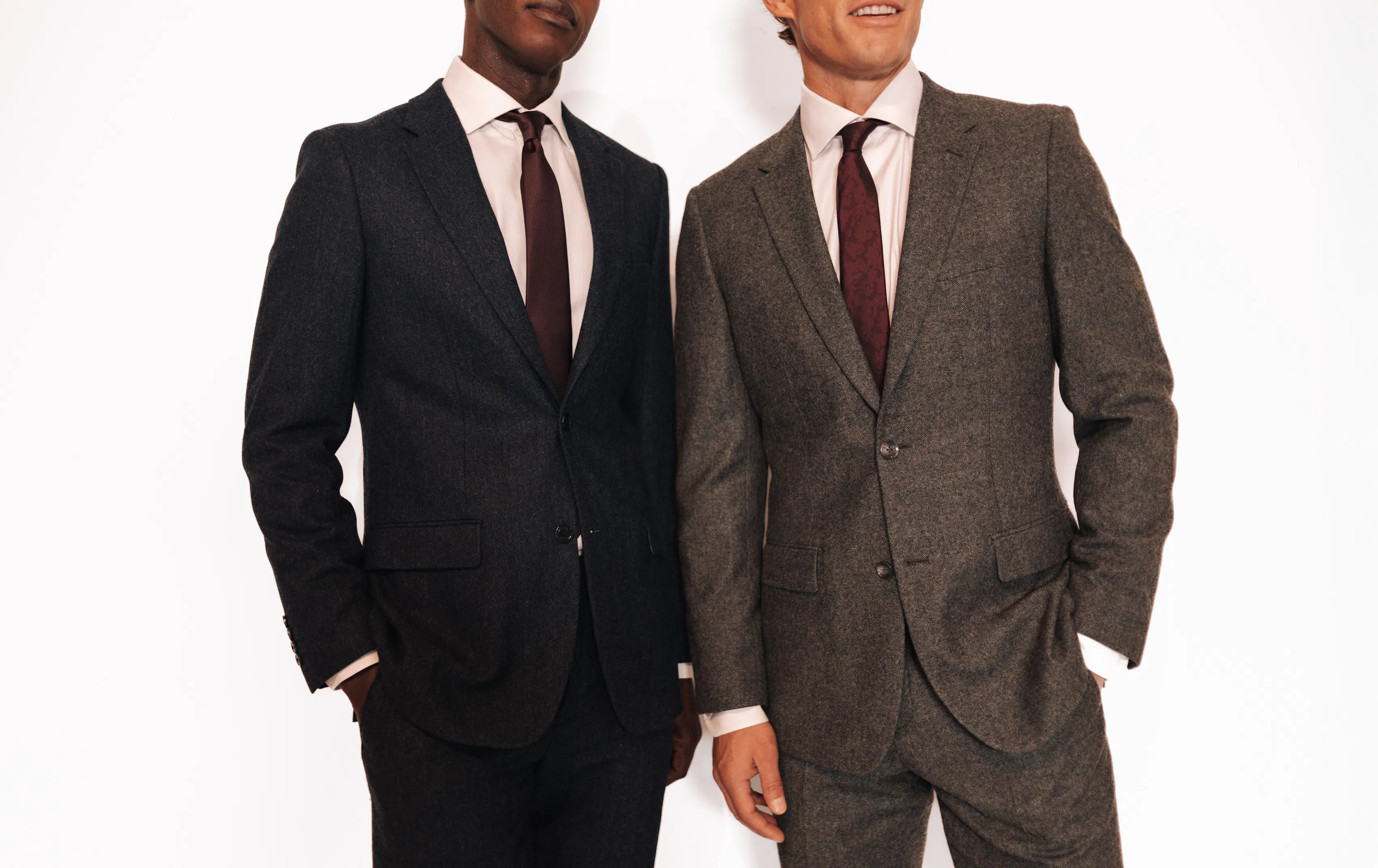Two men, with their faces cropped, stand in full suits next to on another against a white background.