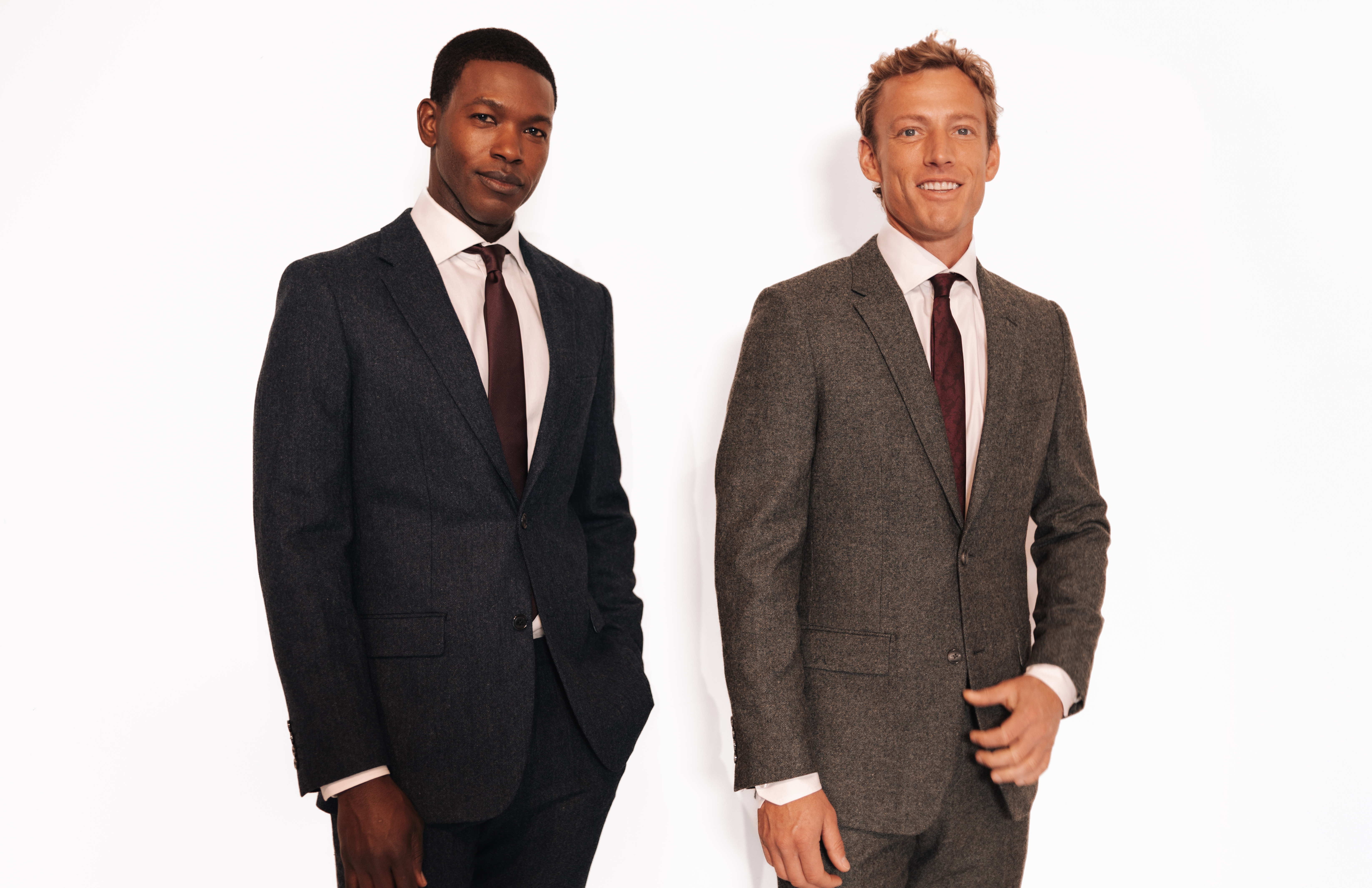 Two men standing side-by-side in suits against a white background.