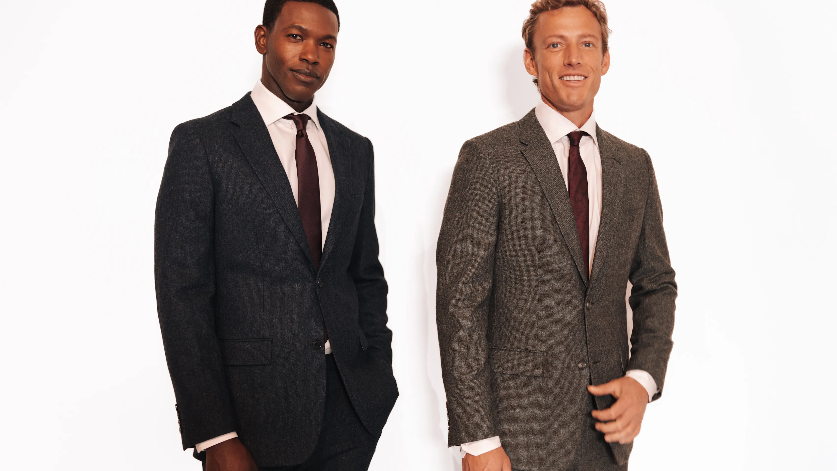 Two men standing side-by-side in suits against a white background.