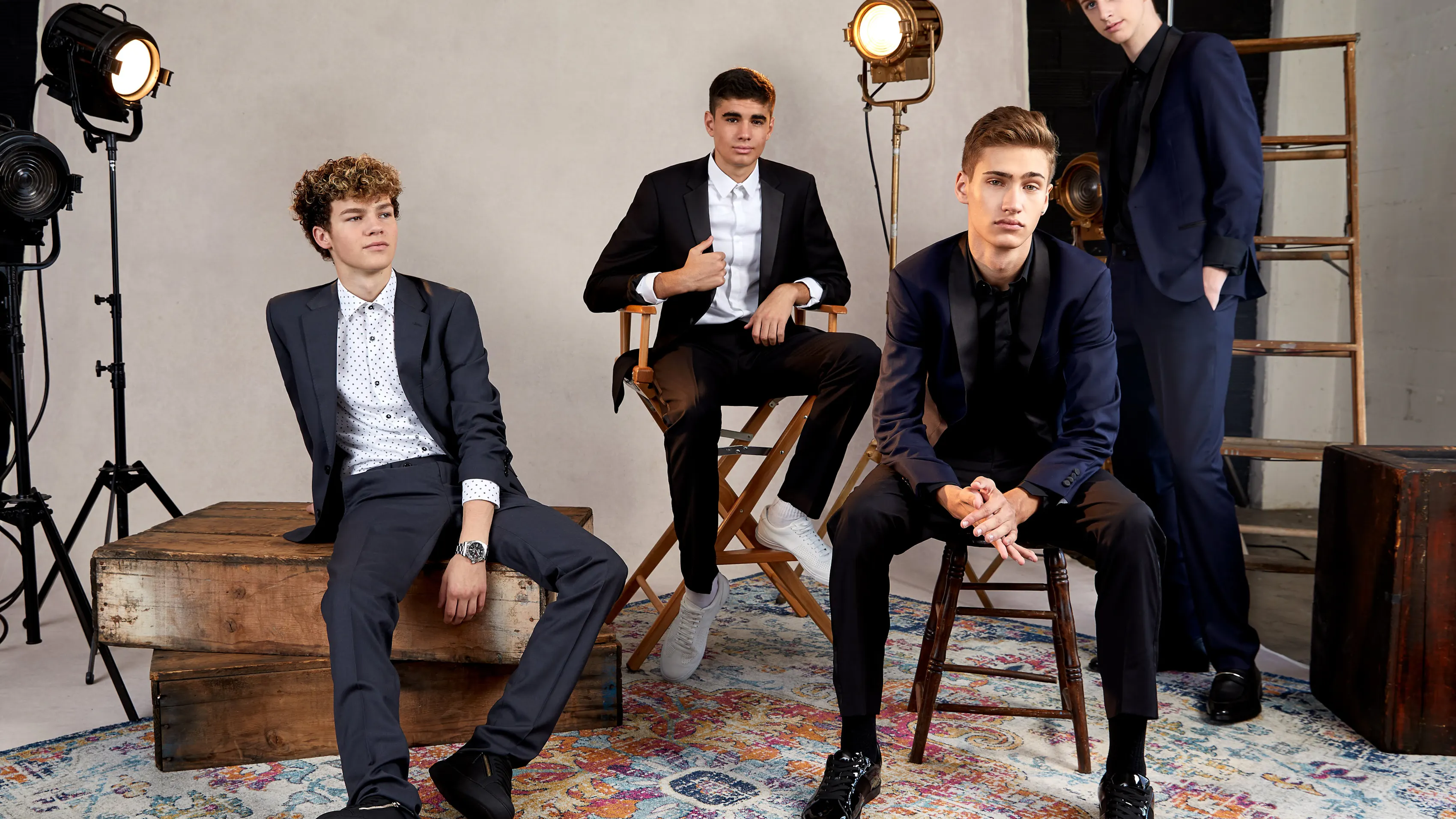 A group of 4 teenage guys post in prom suits on a photoshoot set.