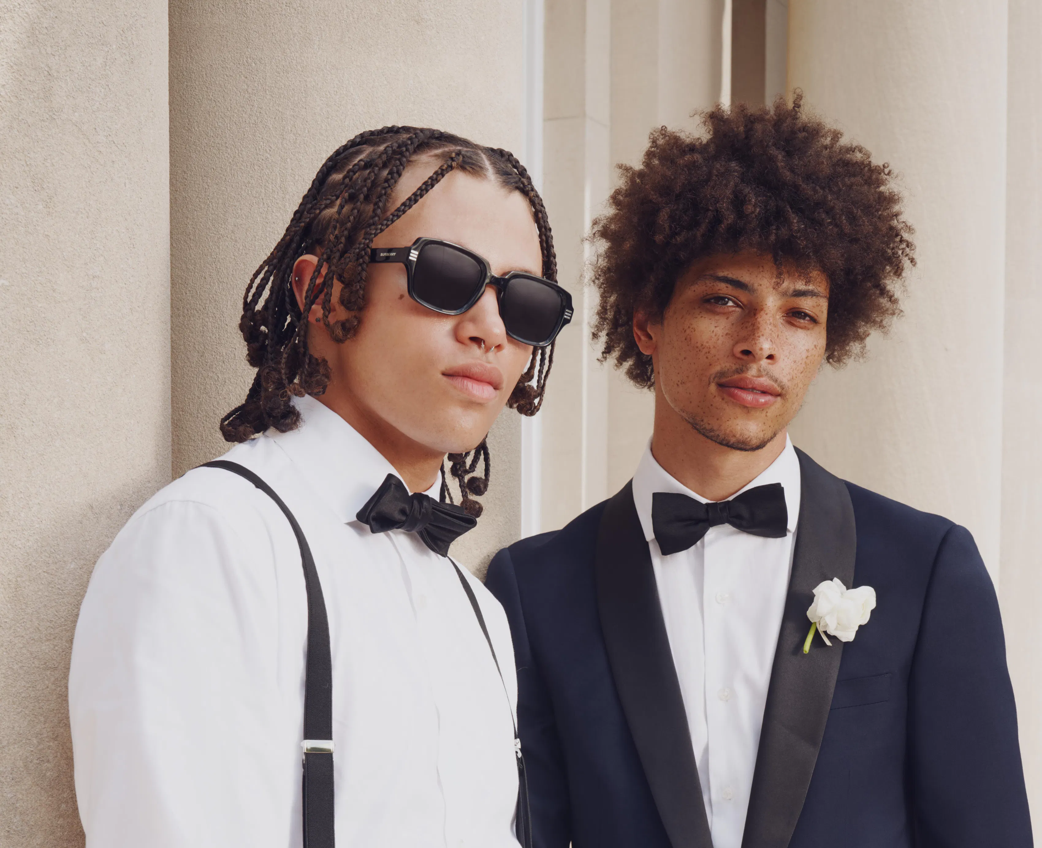 Two teenage guys standing next to eachother in their prom tuxedos.