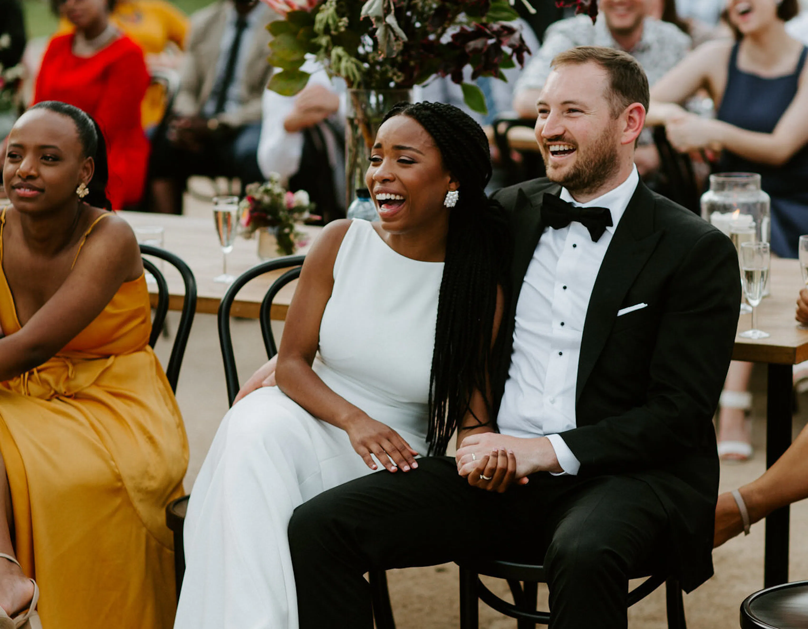 A couple sit and watch a wedding ceremony at a summer wedding.