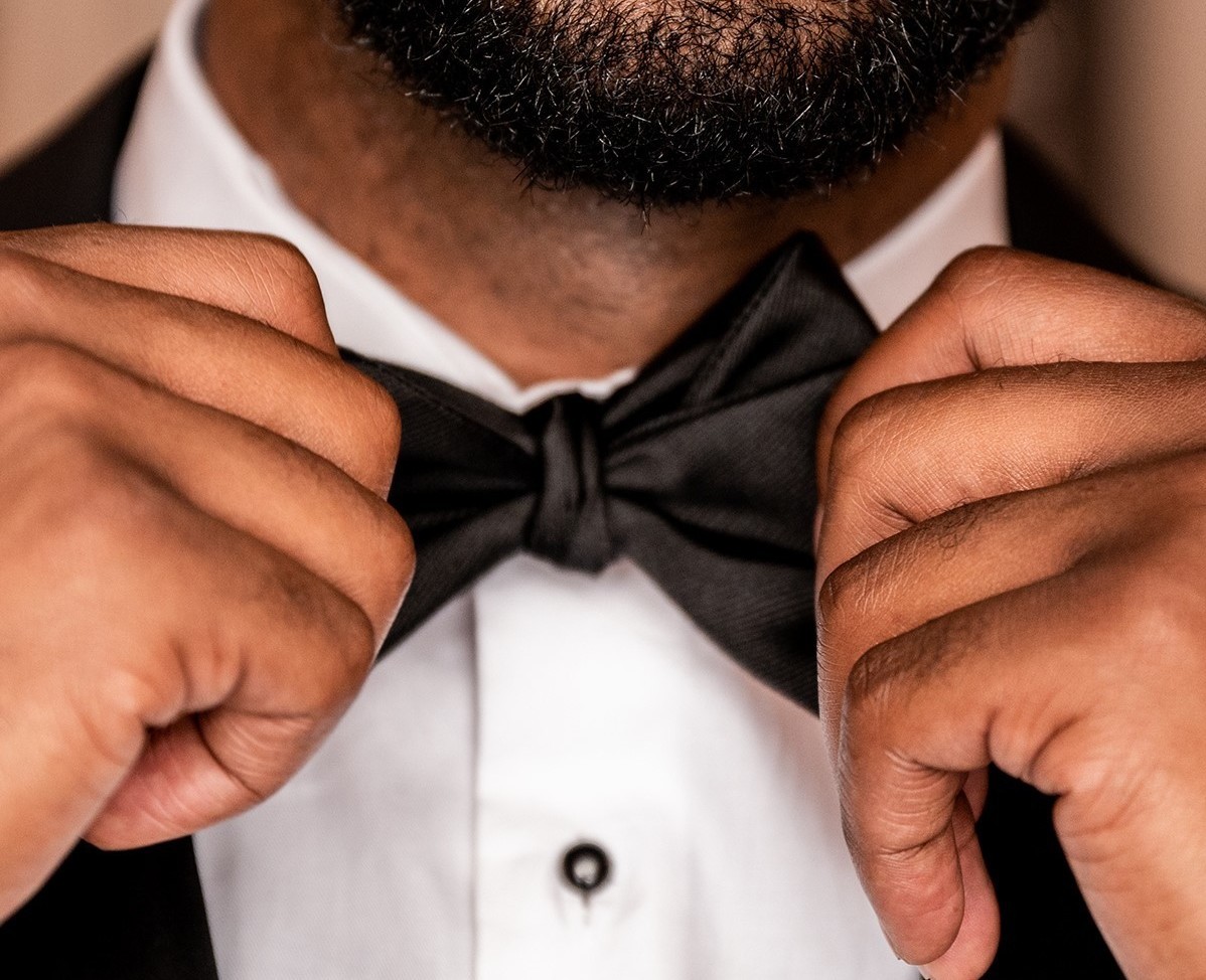 Close-up of a man fastening a bowtie to his tuxedo.