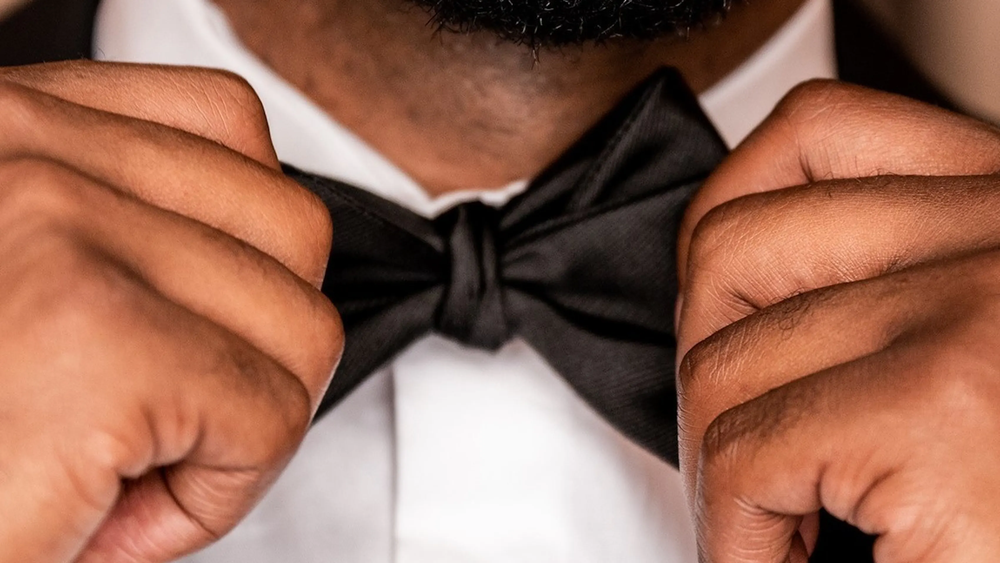 Close-up of a man fastening a bowtie to his tuxedo.