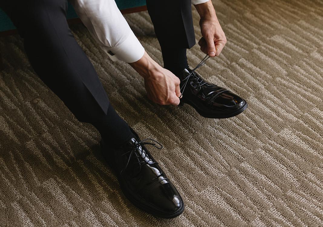 Close-up of a man in a tuxedo tying his shoes before a formal event.