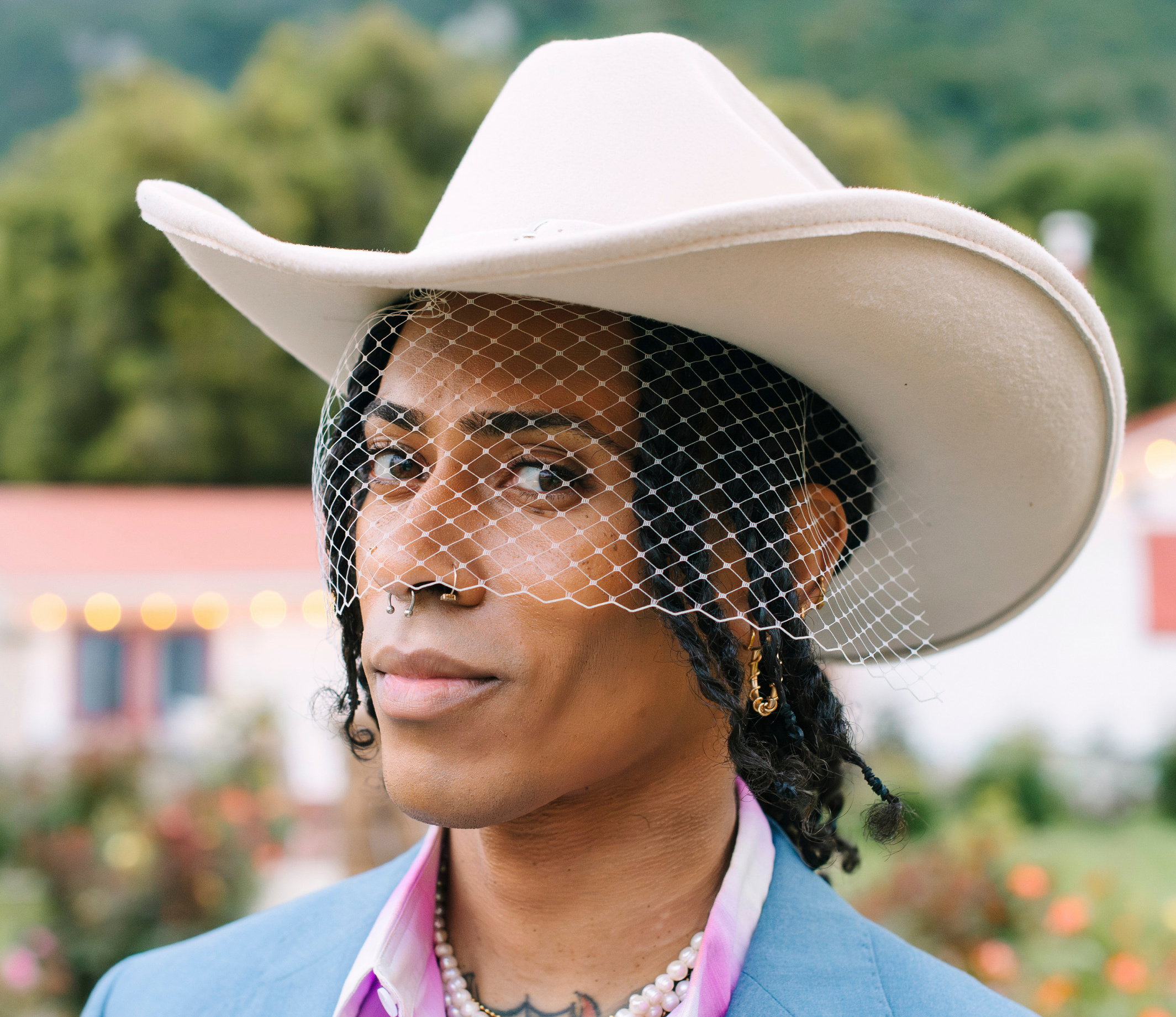 Close-up of a person in a cowboy hat with a face veil on their wedding day.