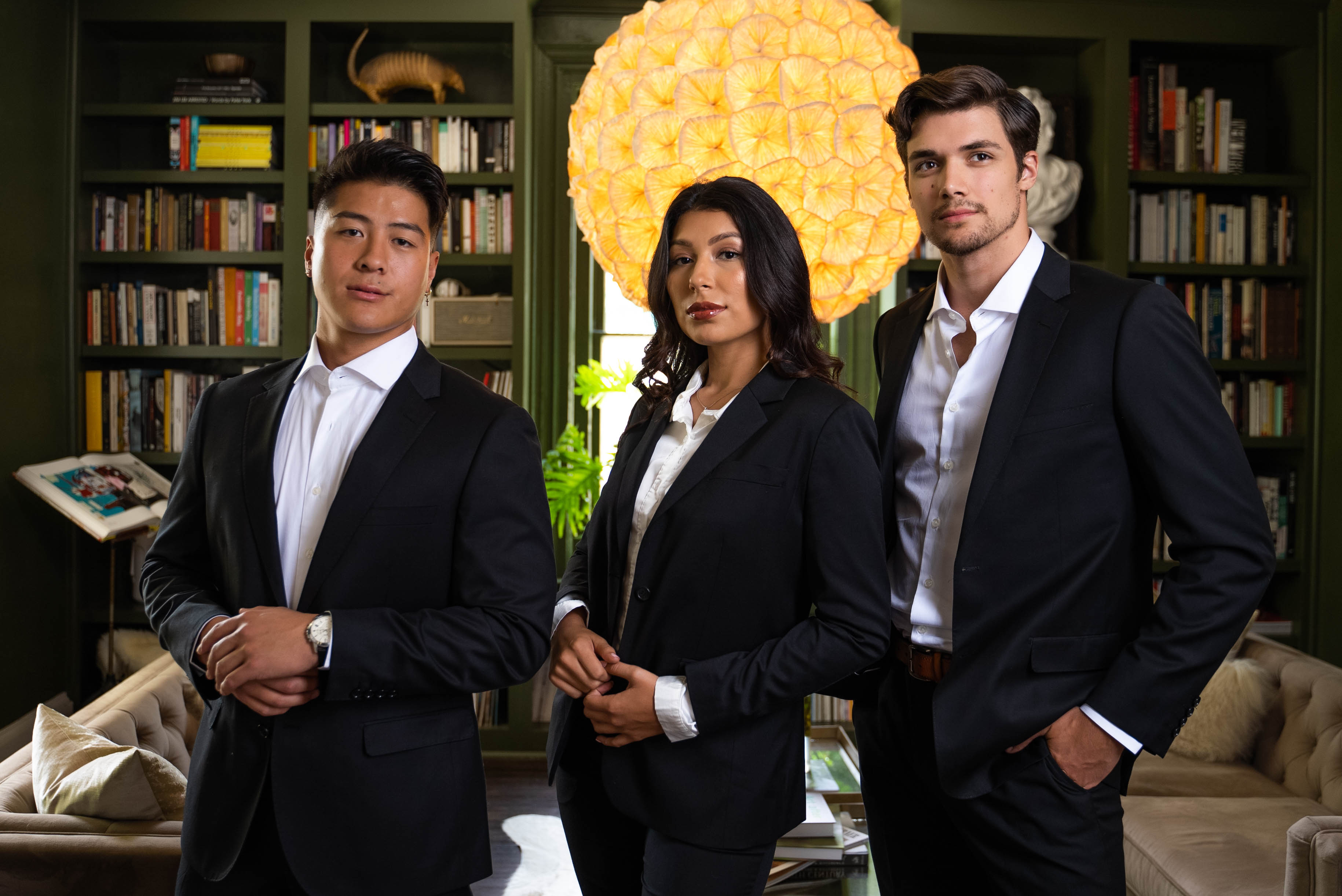 Two men & a woman stand in an office space in suits, all with the top button loose.
