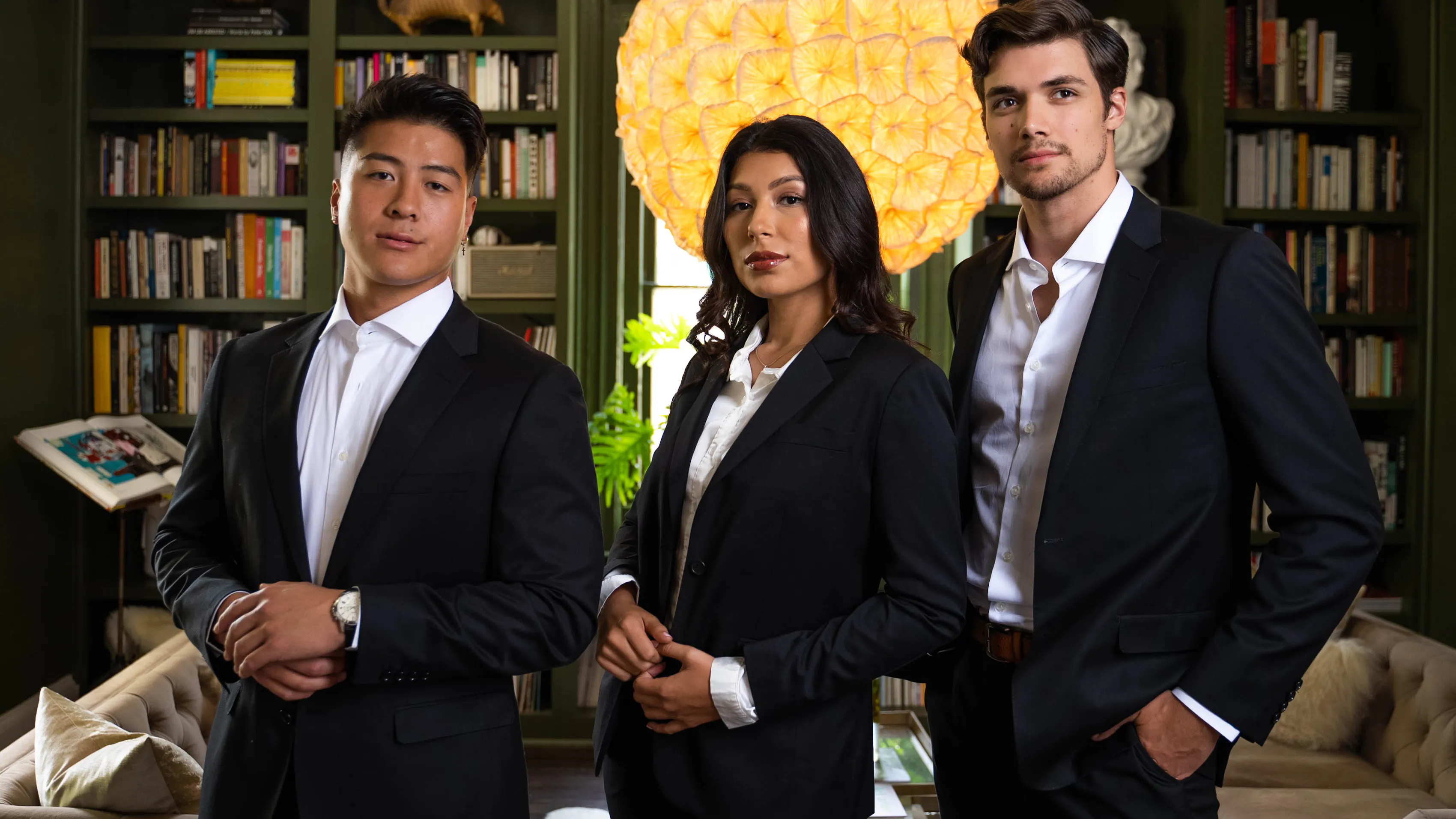 Two men & a woman stand in an office space in suits, all with the top button loose.