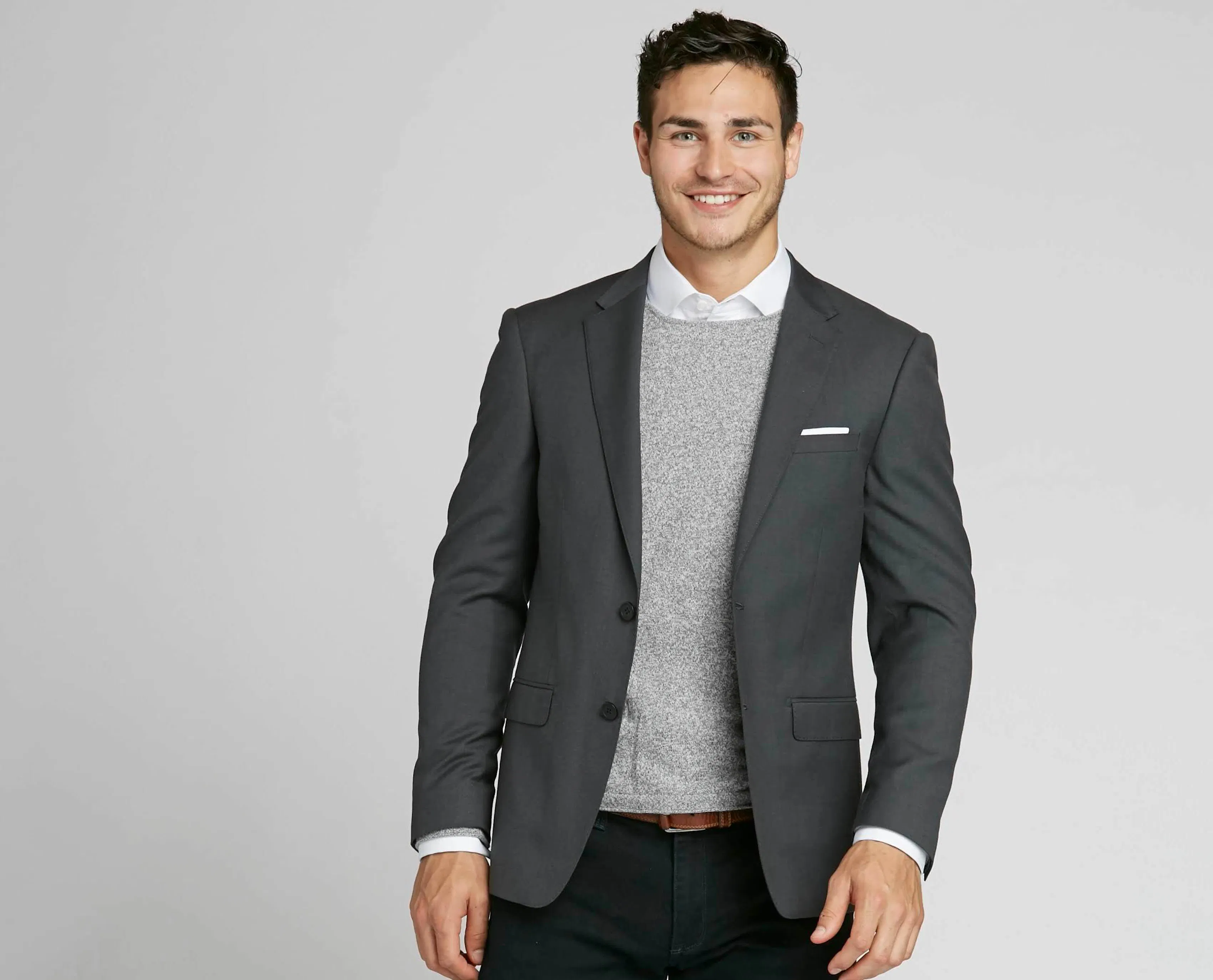 A man dresses down his charcoal suit by layering a grey sweater underneath - perfect for casual weddings.
