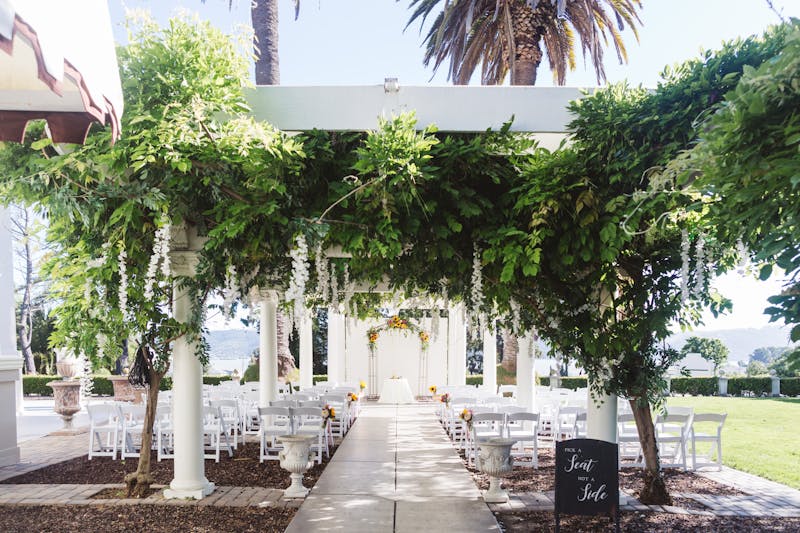 Lush green wedding floral walkway with leafy canopy leading to the outdoor ceremony location